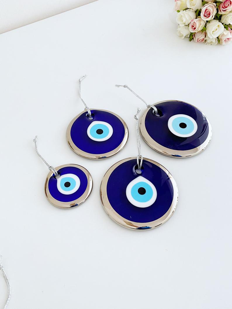 A collection of handmade silver evil eye beads ranging from 7cm to 13cm, showcasing intricate designs and a shiny finish, ready for wall hanging.