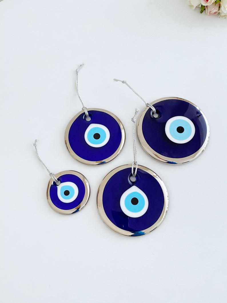 A collection of handmade silver evil eye beads ranging from 7cm to 13cm, showcasing intricate designs and a shiny finish, ready for wall hanging.