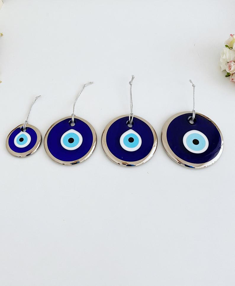 A collection of handmade silver evil eye beads ranging from 7cm to 13cm, showcasing intricate designs and a shiny finish, ready for wall hanging.