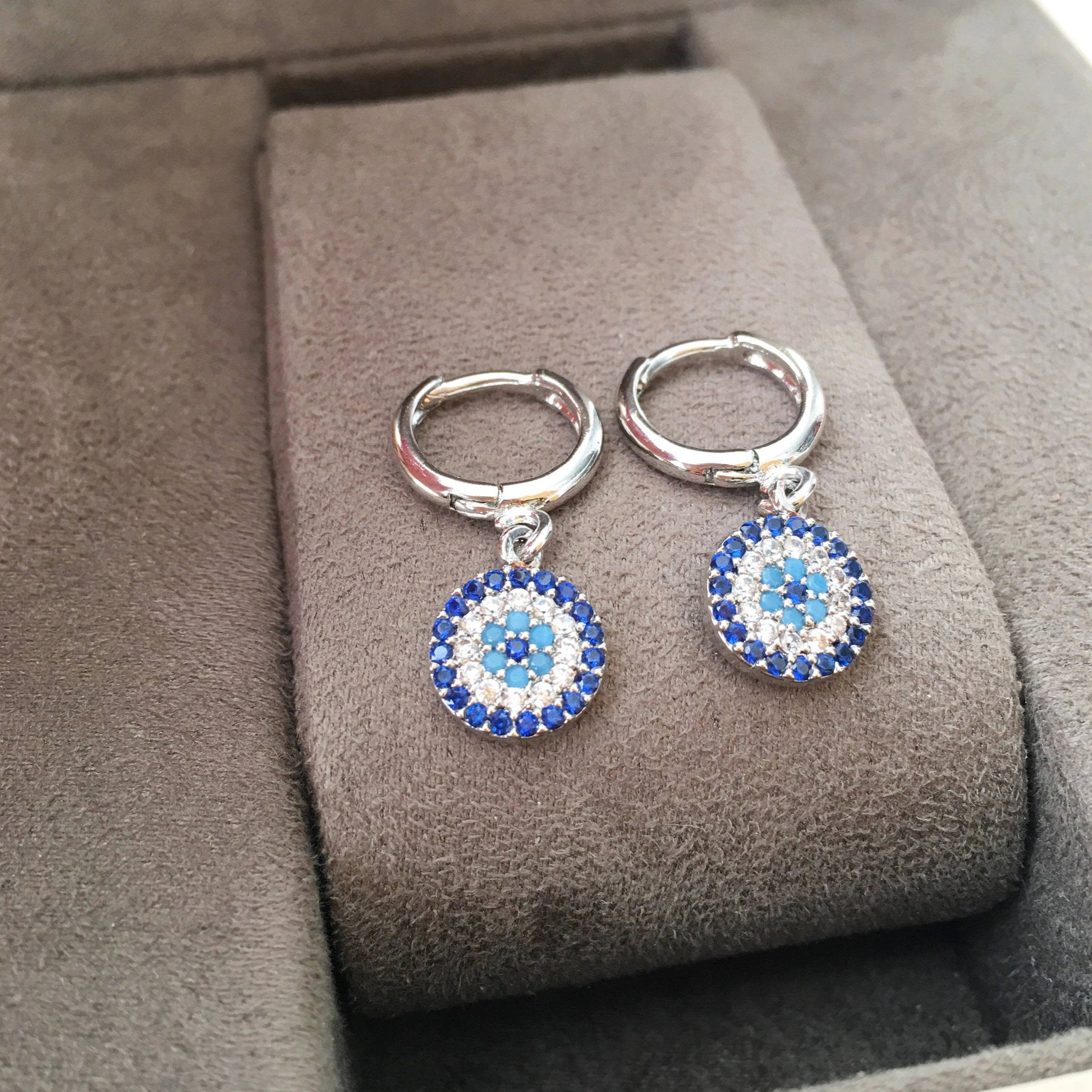 A pair of handmade silver evil eye hoop earrings featuring zircon accents, symbolizing protection and good luck.