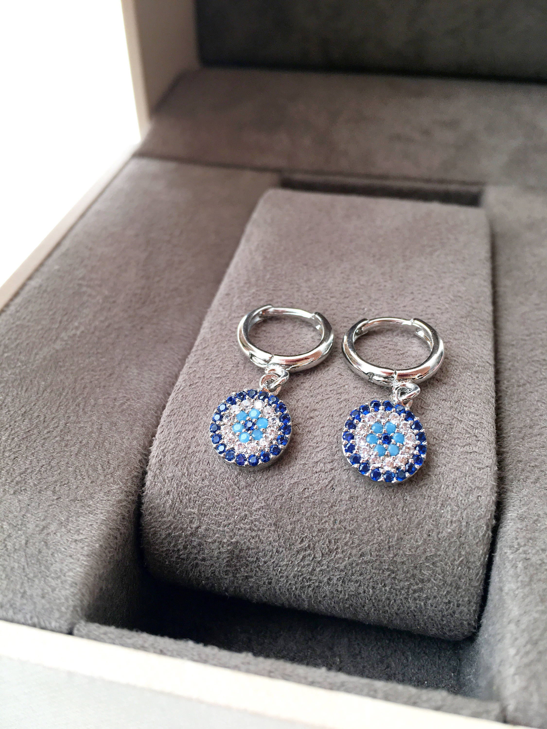 A pair of handmade silver evil eye hoop earrings featuring zircon accents, symbolizing protection and good luck.