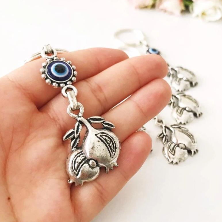 A beautiful silver keychain featuring a pomegranate design with an evil eye symbol, perfect for good luck and charm.