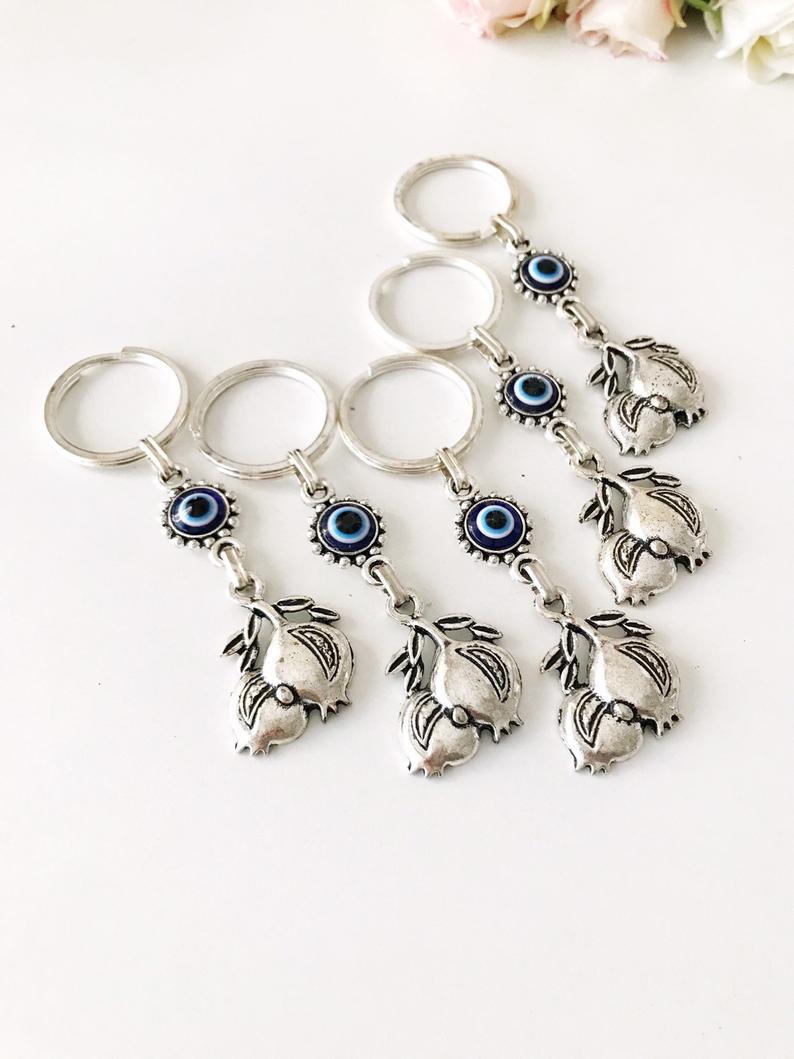 A beautiful silver keychain featuring a pomegranate design with an evil eye symbol, perfect for good luck and charm.