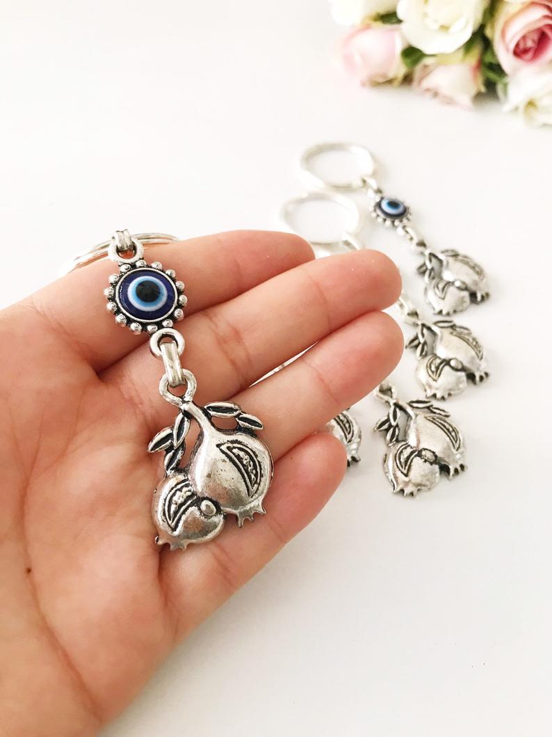 A beautiful silver keychain featuring a pomegranate design with an evil eye symbol, perfect for good luck and charm.