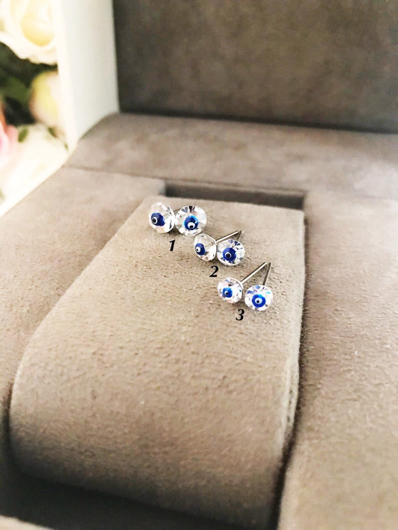 A pair of handmade silver evil eye stud earrings featuring a minimalist design with crystal accents, symbolizing protection.