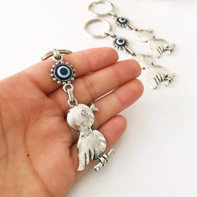 A silver keychain featuring a bird charm and a blue evil eye, symbolizing protection and luck.