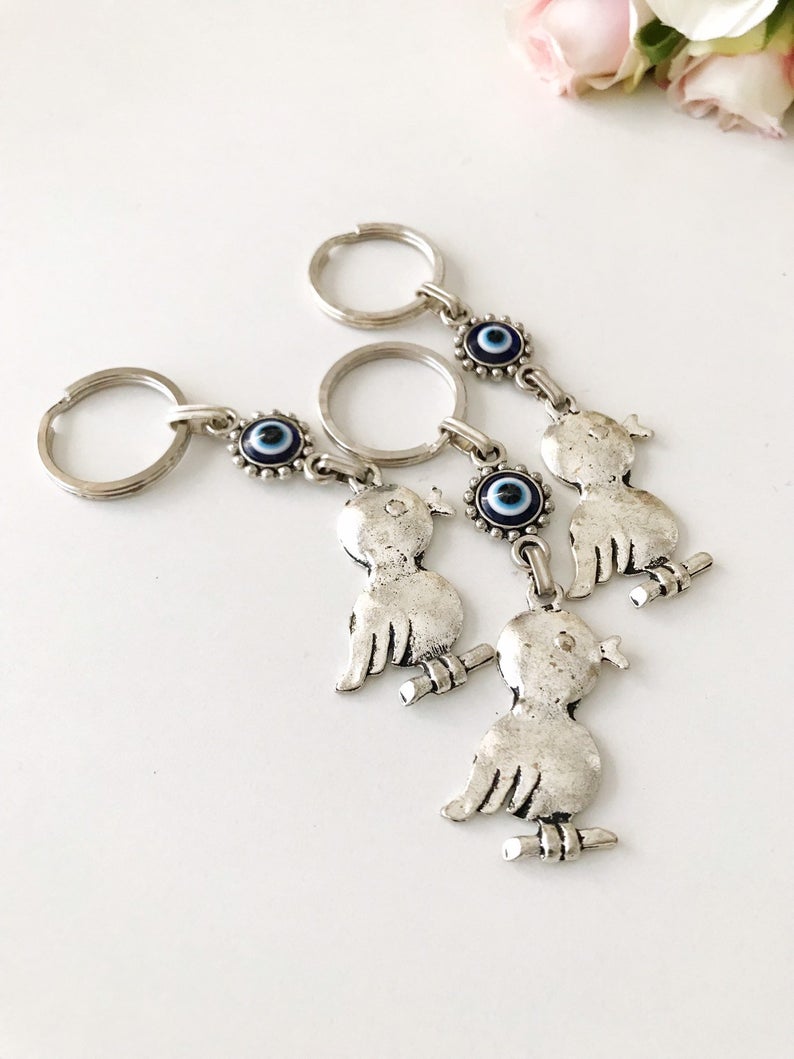 A silver keychain featuring a bird charm and a blue evil eye, symbolizing protection and luck.