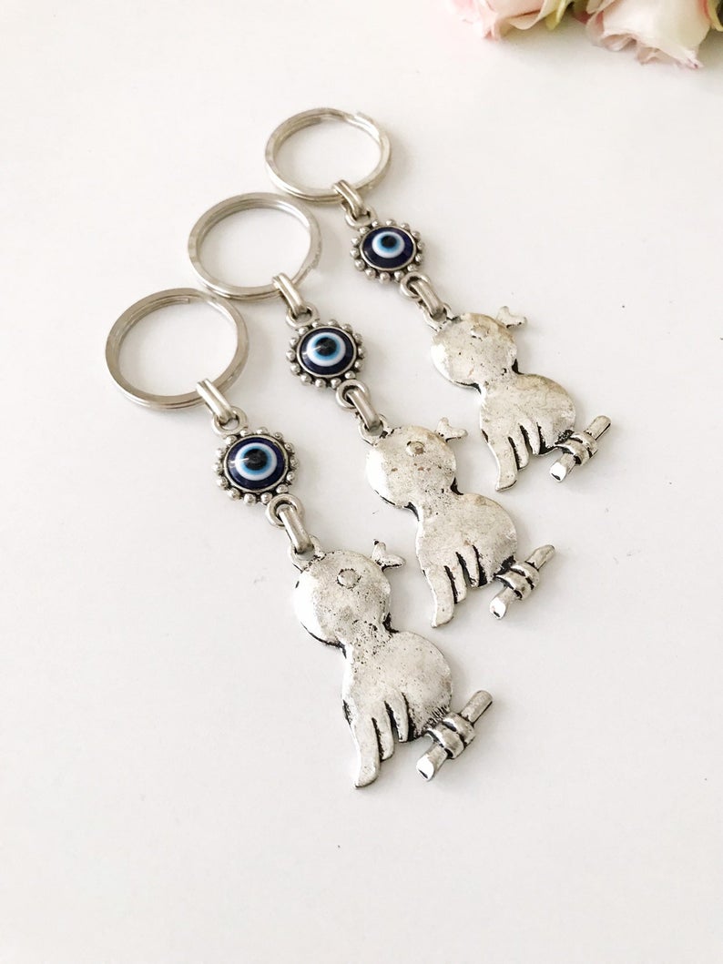 A silver keychain featuring a bird charm and a blue evil eye, symbolizing protection and luck.