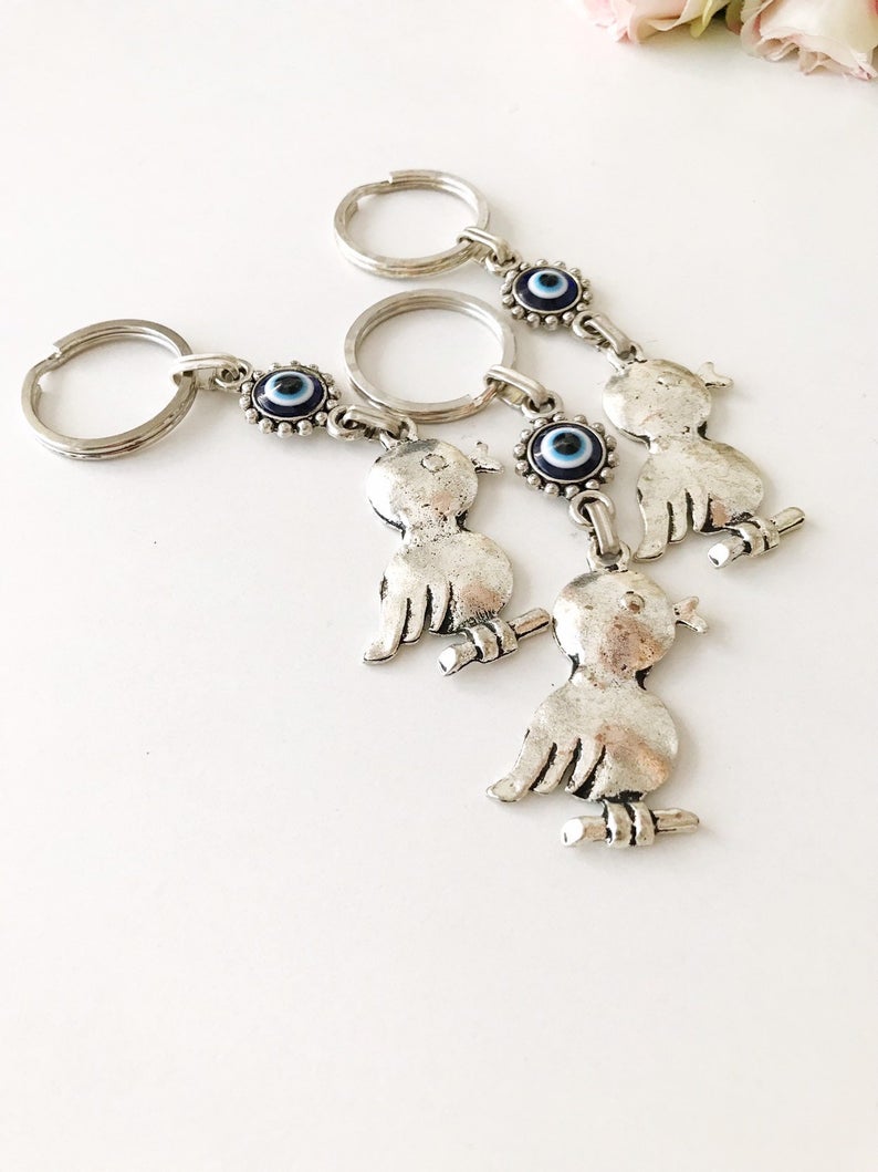 A silver keychain featuring a bird charm and a blue evil eye, symbolizing protection and luck.