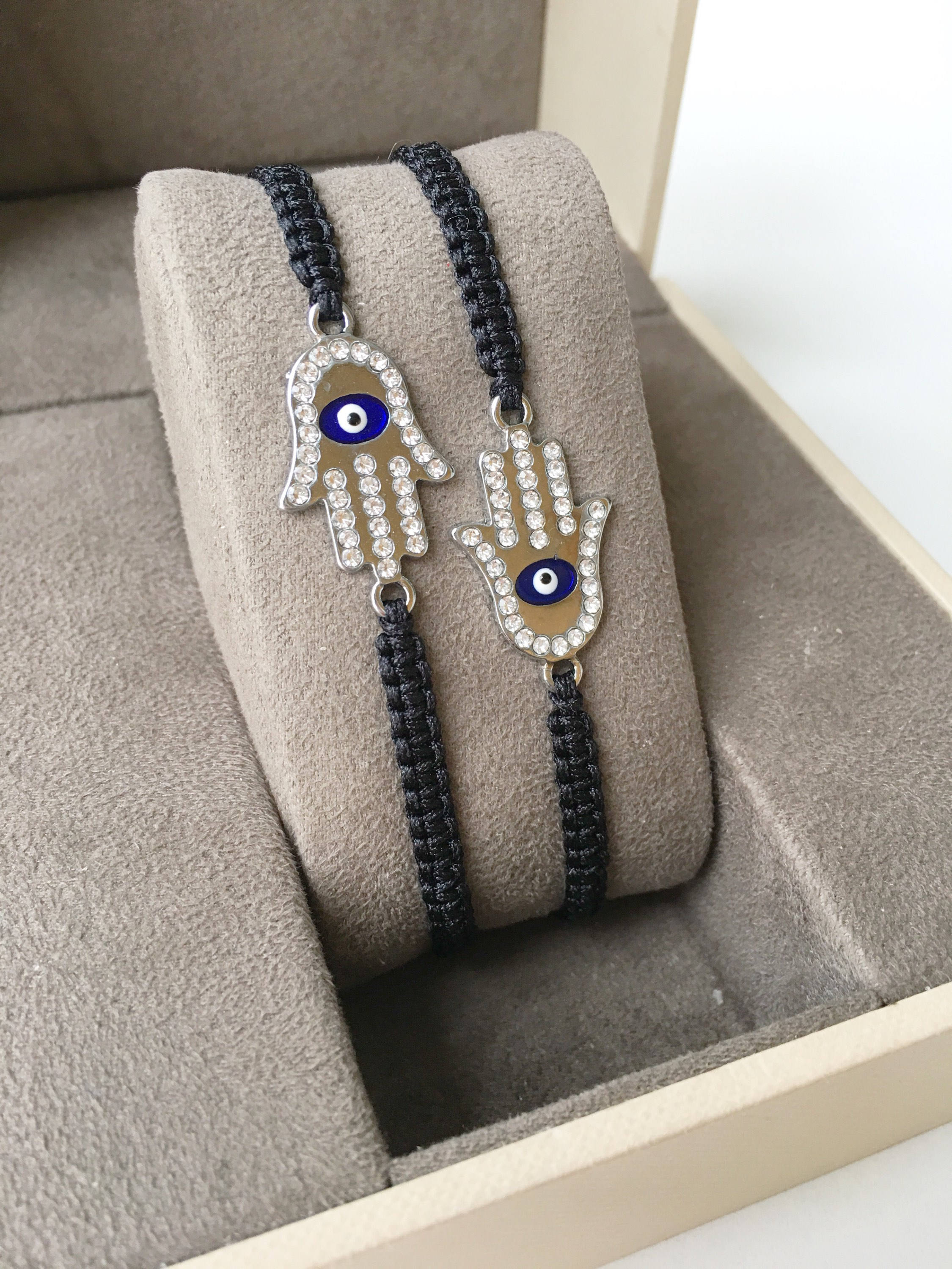 A handmade Silver Hamsa Evil Eye Bracelet featuring a silver zirconia hamsa charm on an adjustable black macrame string.