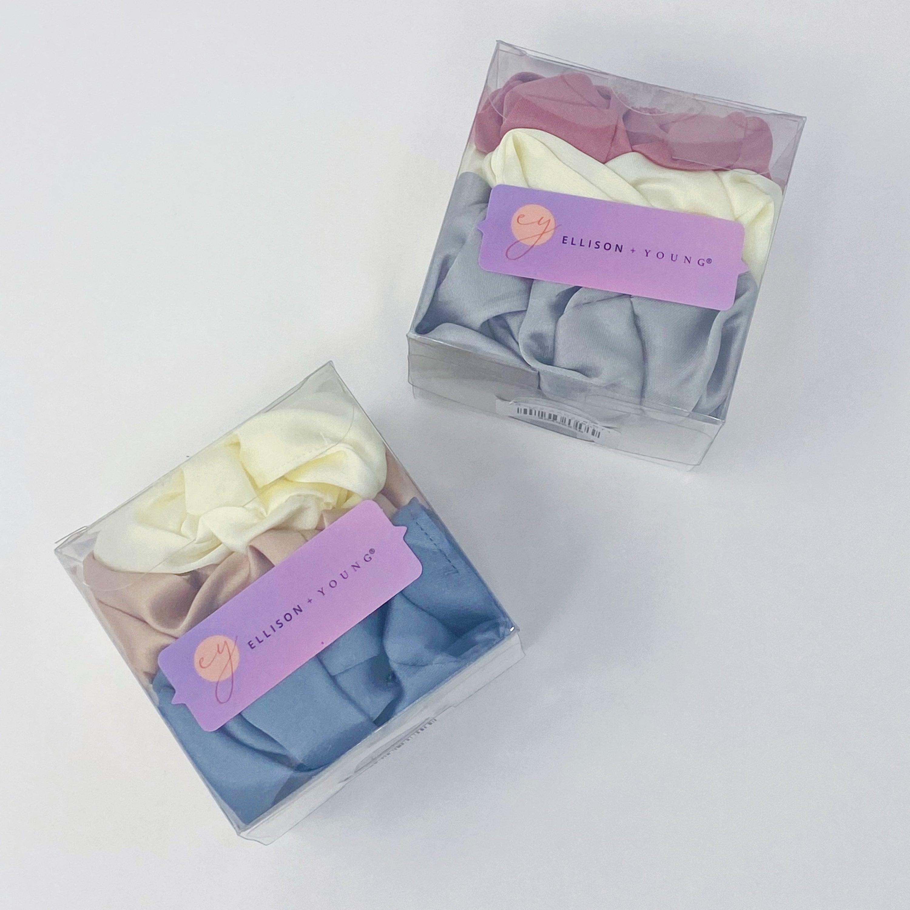 Set of 3 soft satin scrunchies in various colors, elegantly packaged in a clear cello case with Ellison + Young branding.