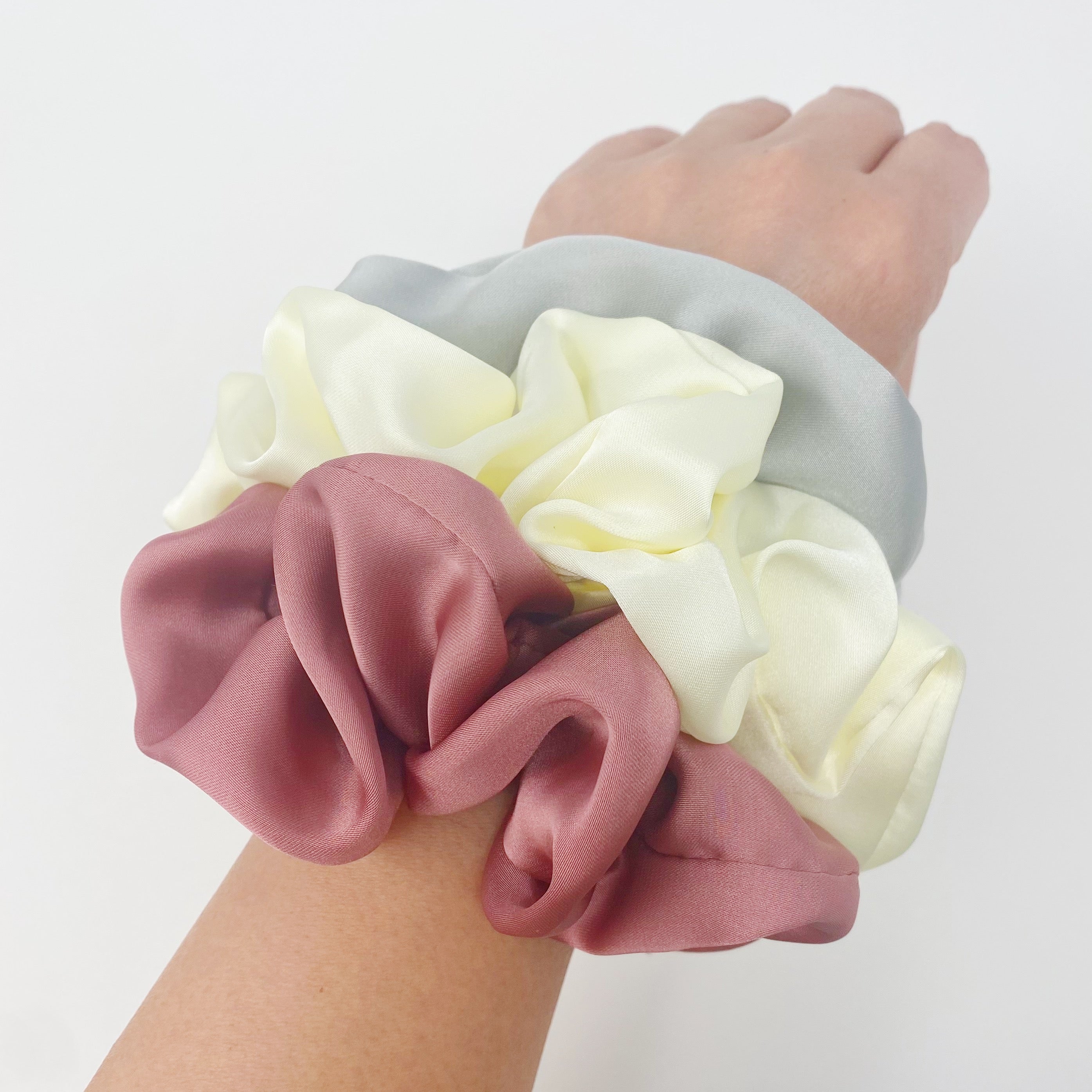 Set of 3 soft satin scrunchies in various colors, elegantly packaged in a clear cello case with Ellison + Young branding.