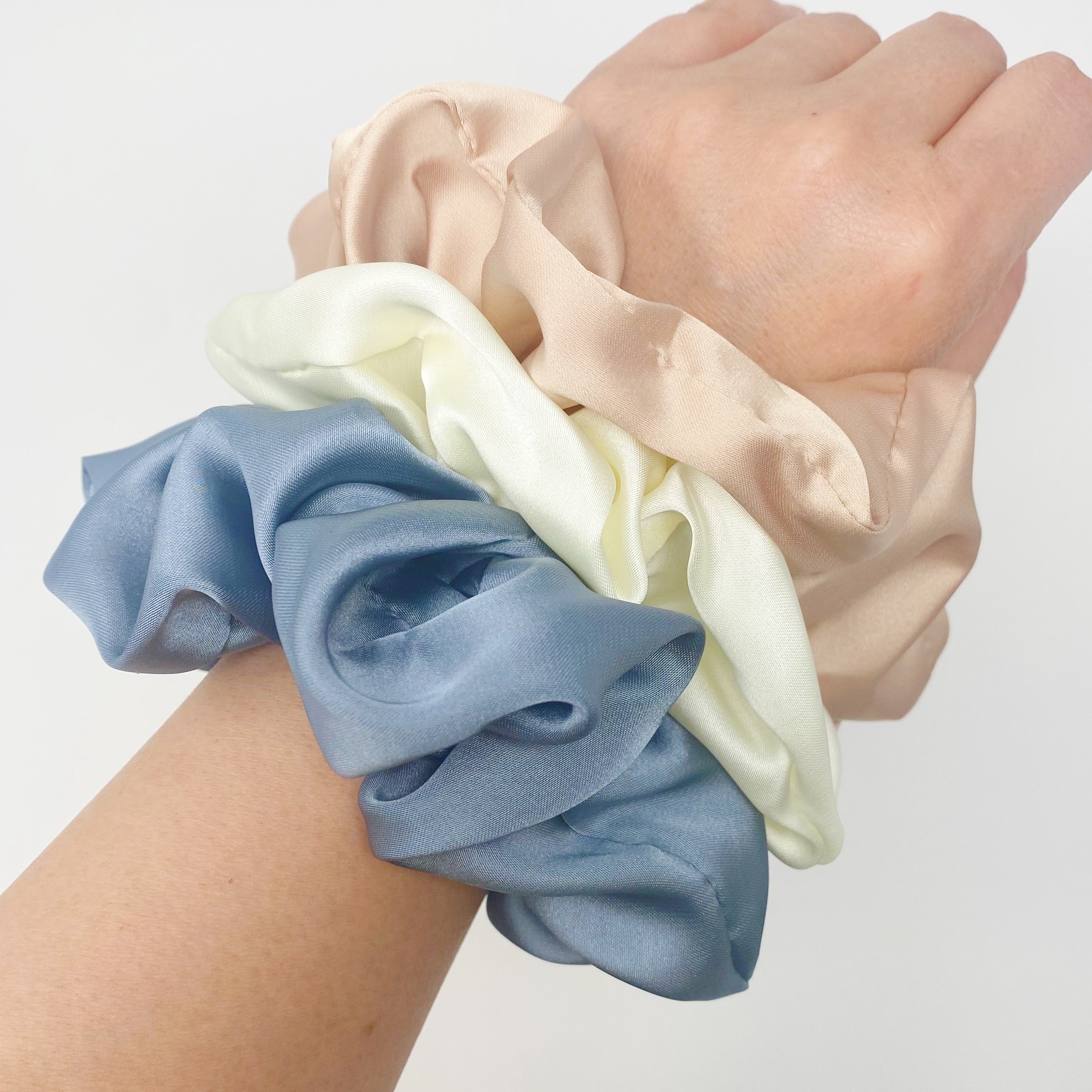 Set of 3 soft satin scrunchies in various colors, elegantly packaged in a clear cello case with Ellison + Young branding.