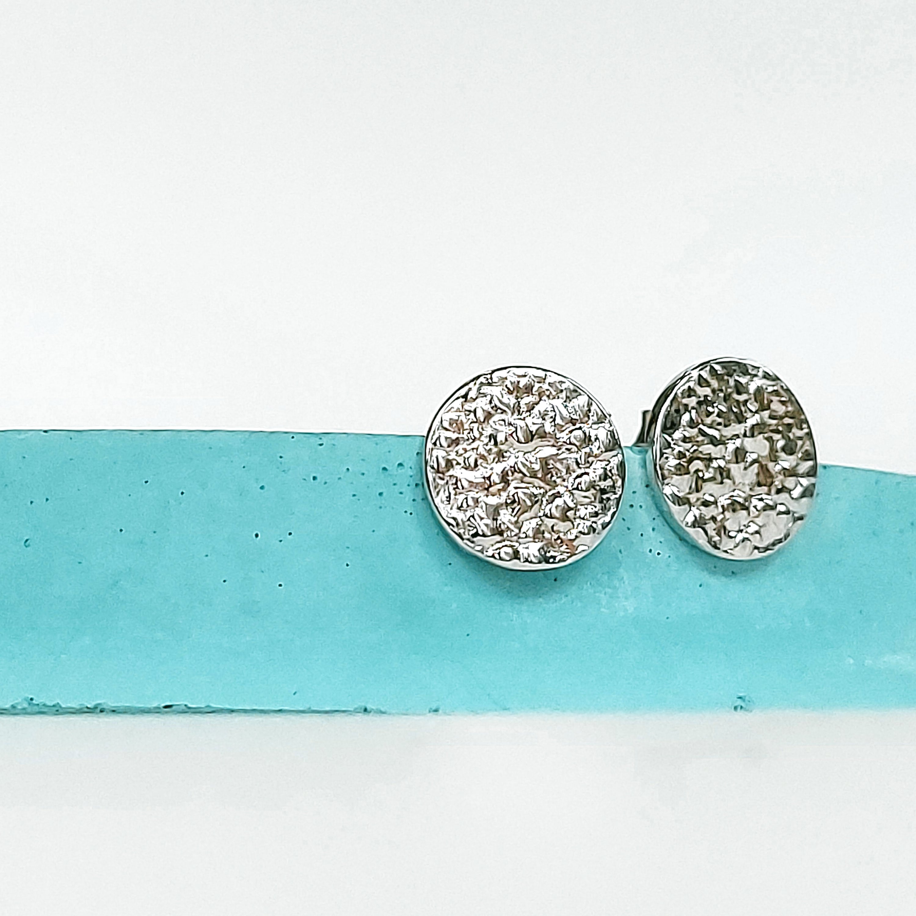 A pair of small textured circle stud earrings made of 925 sterling silver, showcasing their sparkling design and available finishes.