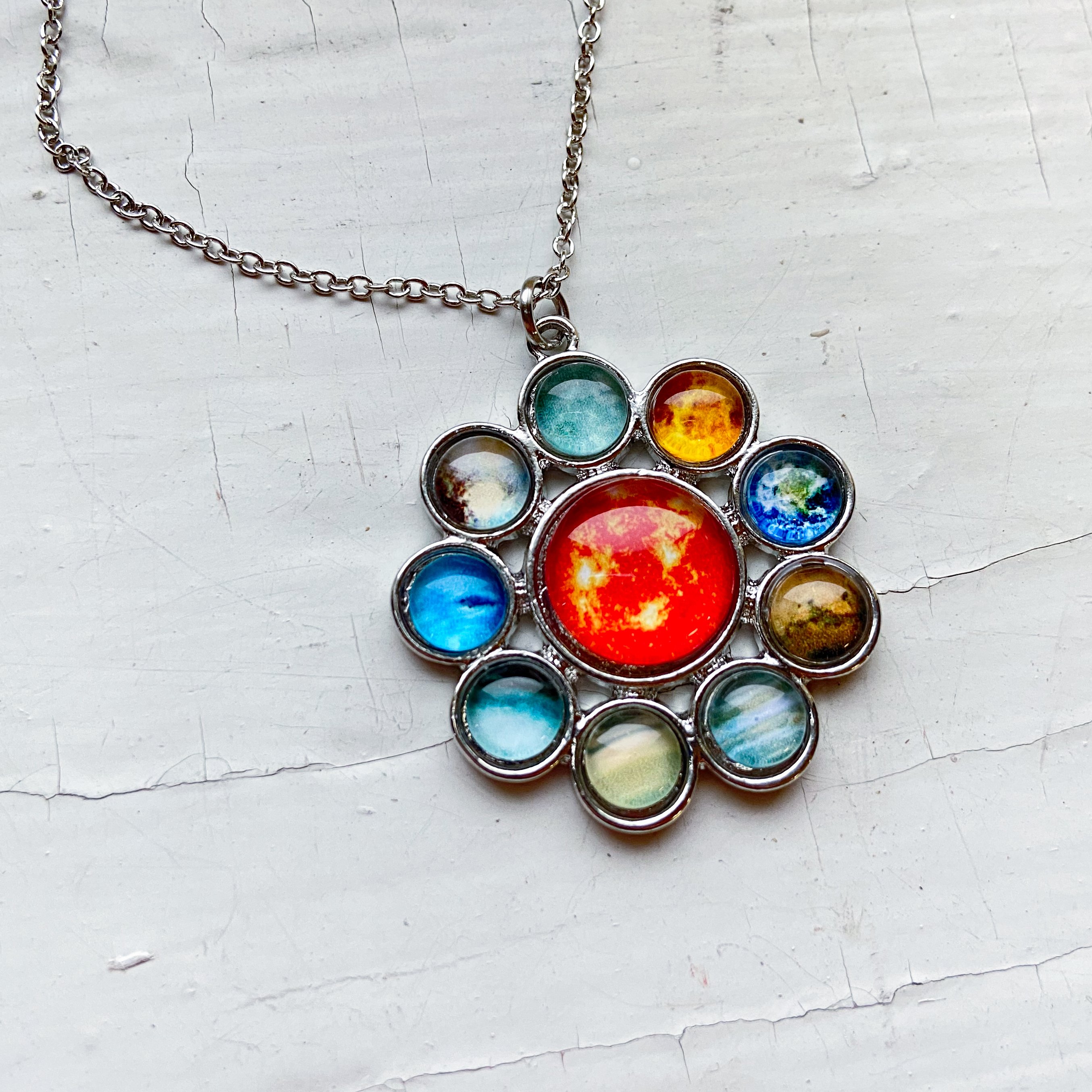 A colorful Solar System Halo Pendant featuring the Sun and all planets, handcrafted in rhodium plated brass.