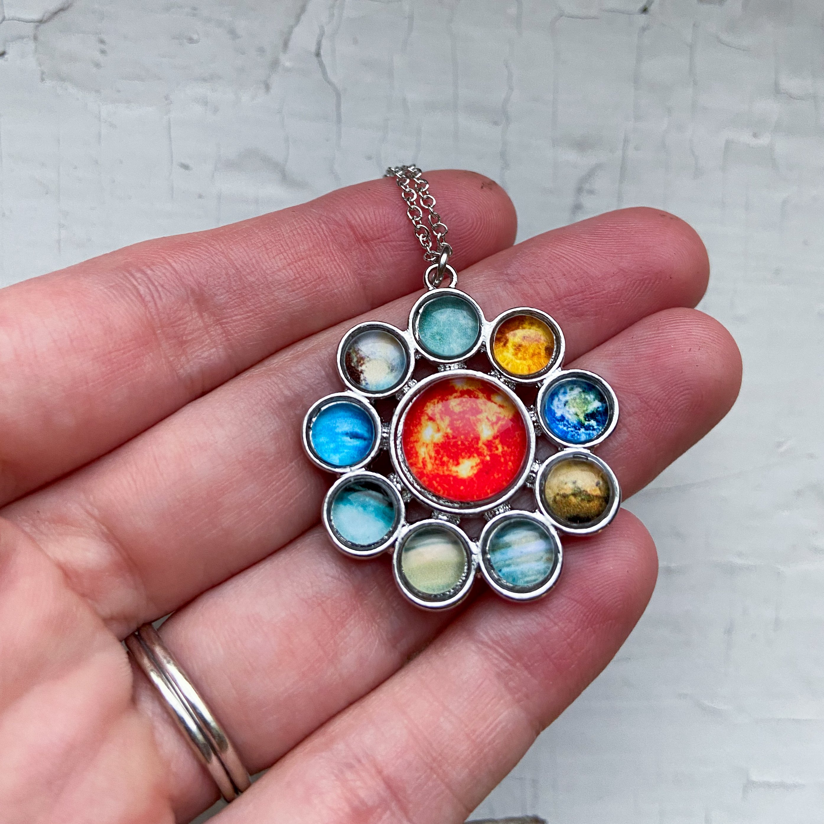 A colorful Solar System Halo Pendant featuring the Sun and all planets, handcrafted in rhodium plated brass.