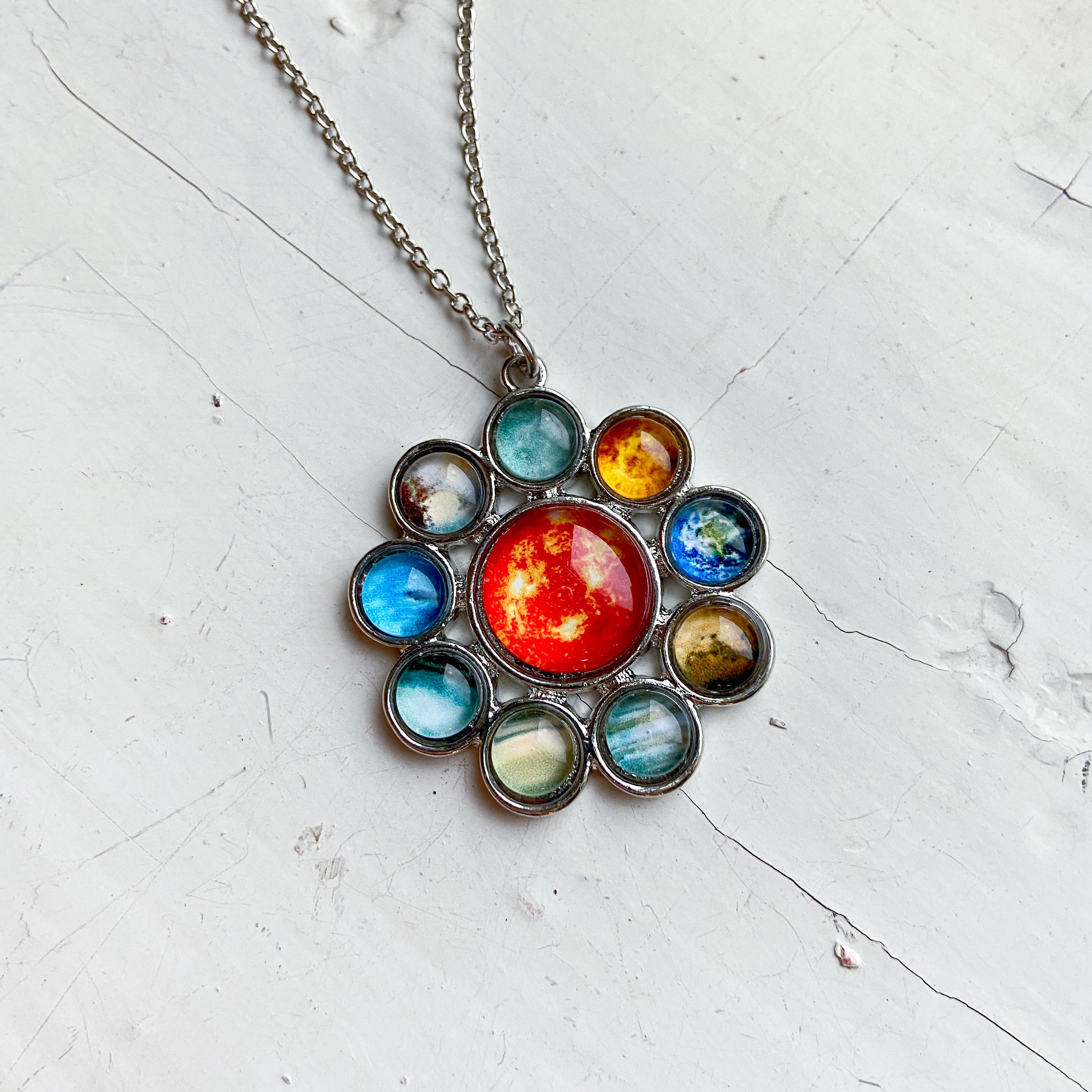 A colorful Solar System Halo Pendant featuring the Sun and all planets, handcrafted in rhodium plated brass.