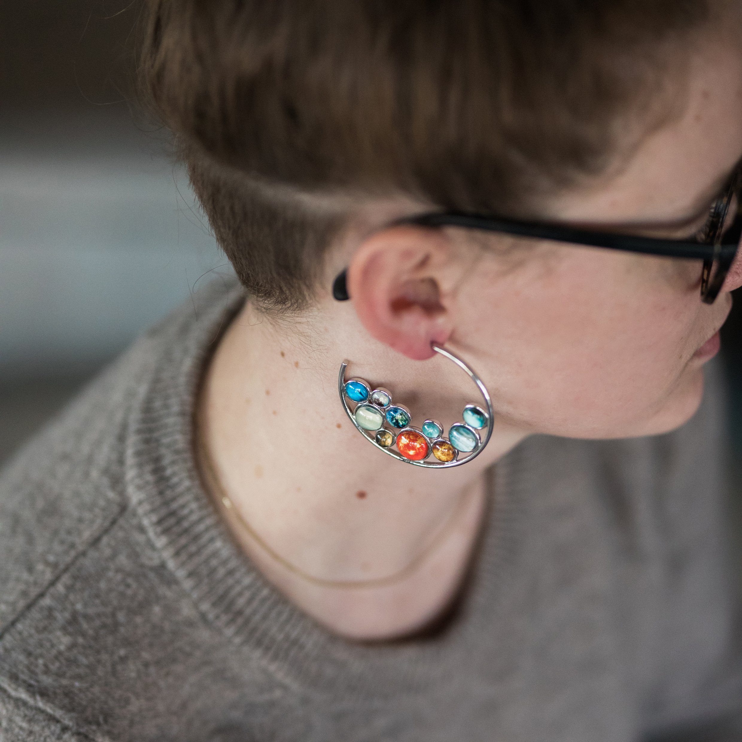 A pair of handcrafted Solar System Hoop Earrings featuring colorful planets and the Sun, set in a silver-tone design with a textured metal back.