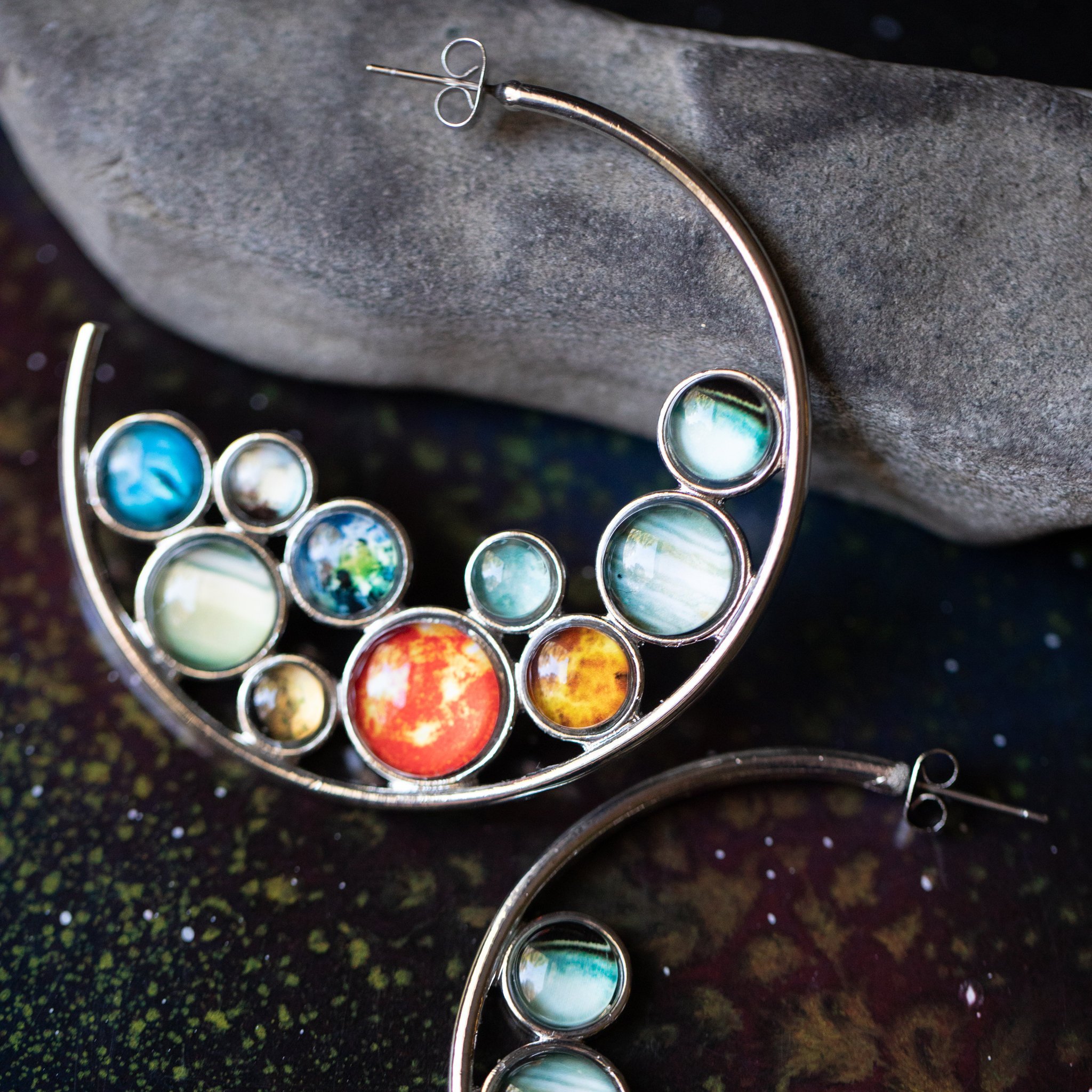 A pair of handcrafted Solar System Hoop Earrings featuring colorful planets and the Sun, set in a silver-tone design with a textured metal back.