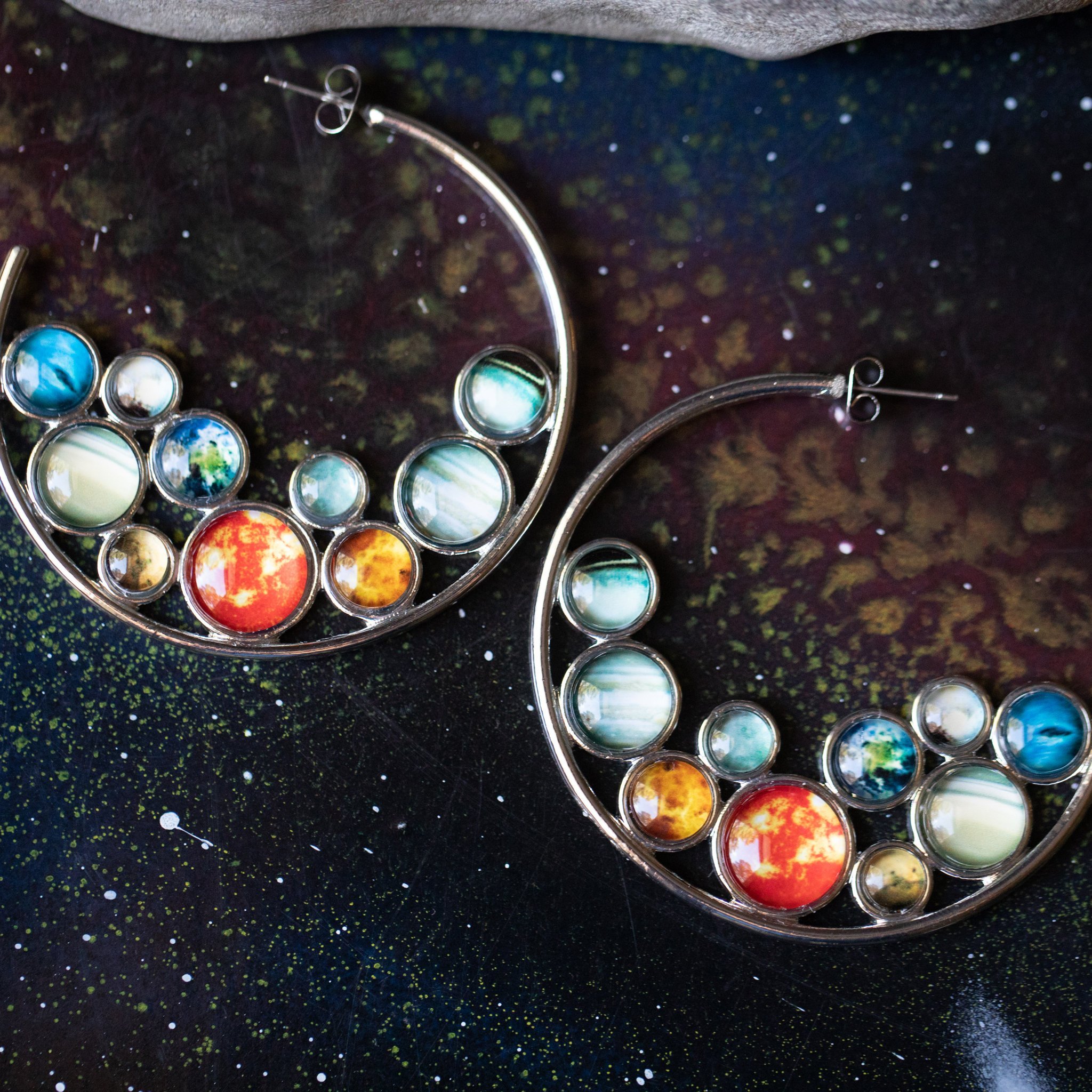 A pair of handcrafted Solar System Hoop Earrings featuring colorful planets and the Sun, set in a silver-tone design with a textured metal back.