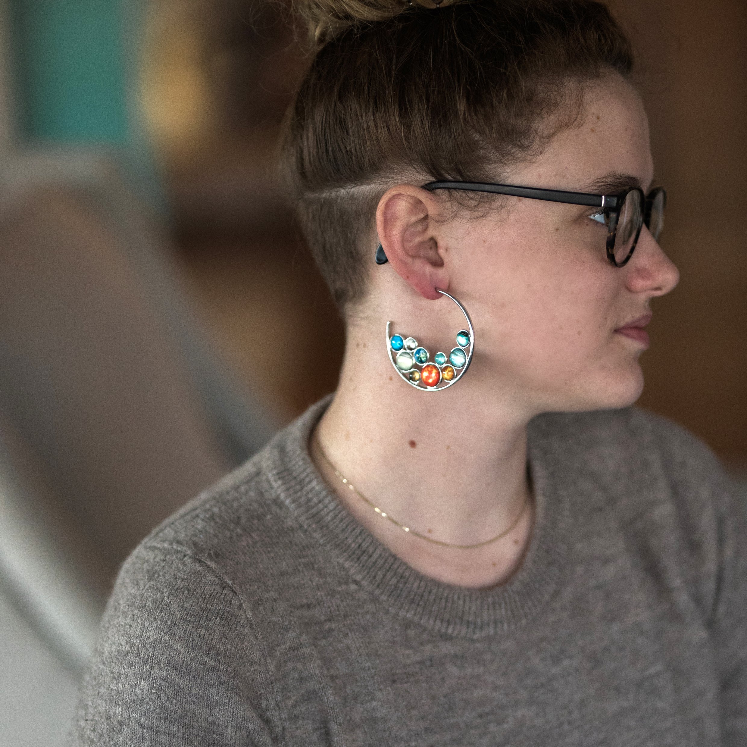 A pair of handcrafted Solar System Hoop Earrings featuring colorful planets and the Sun, set in a silver-tone design with a textured metal back.