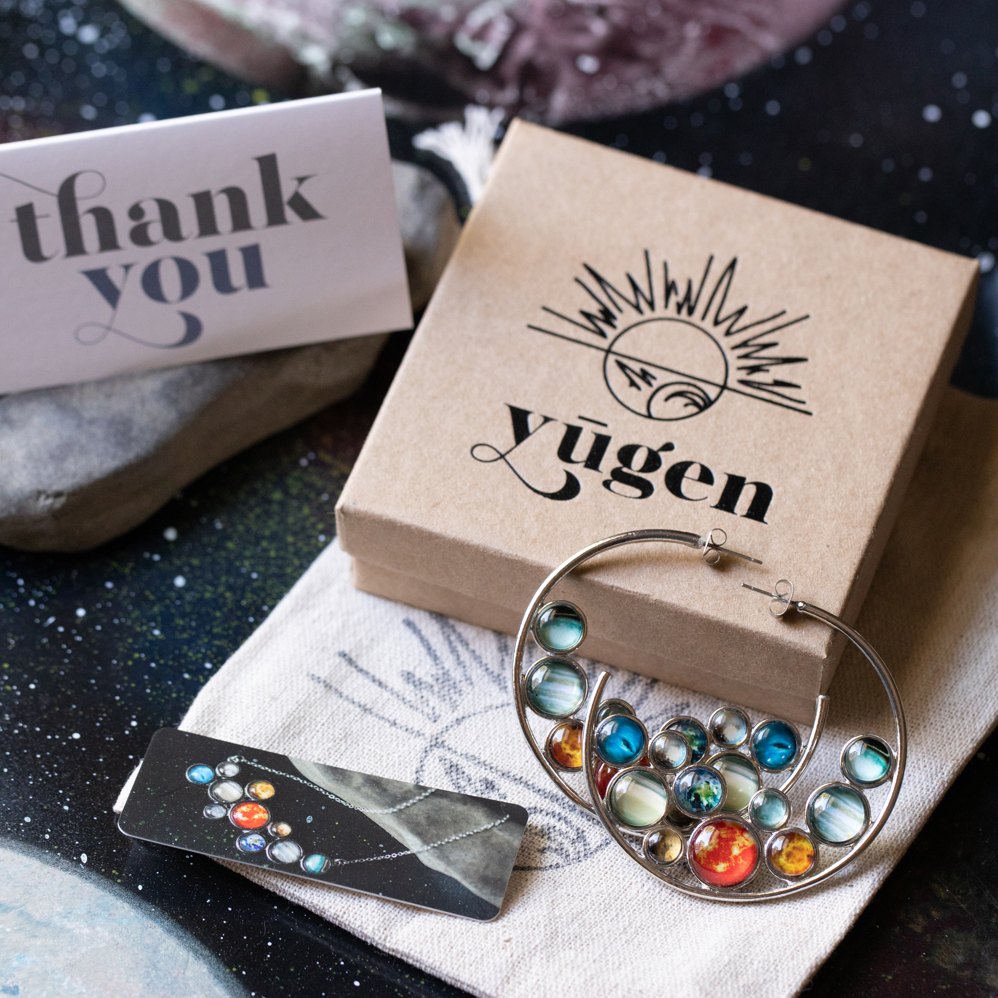 A pair of handcrafted Solar System Hoop Earrings featuring colorful planets and the Sun, set in a silver-tone design with a textured metal back.