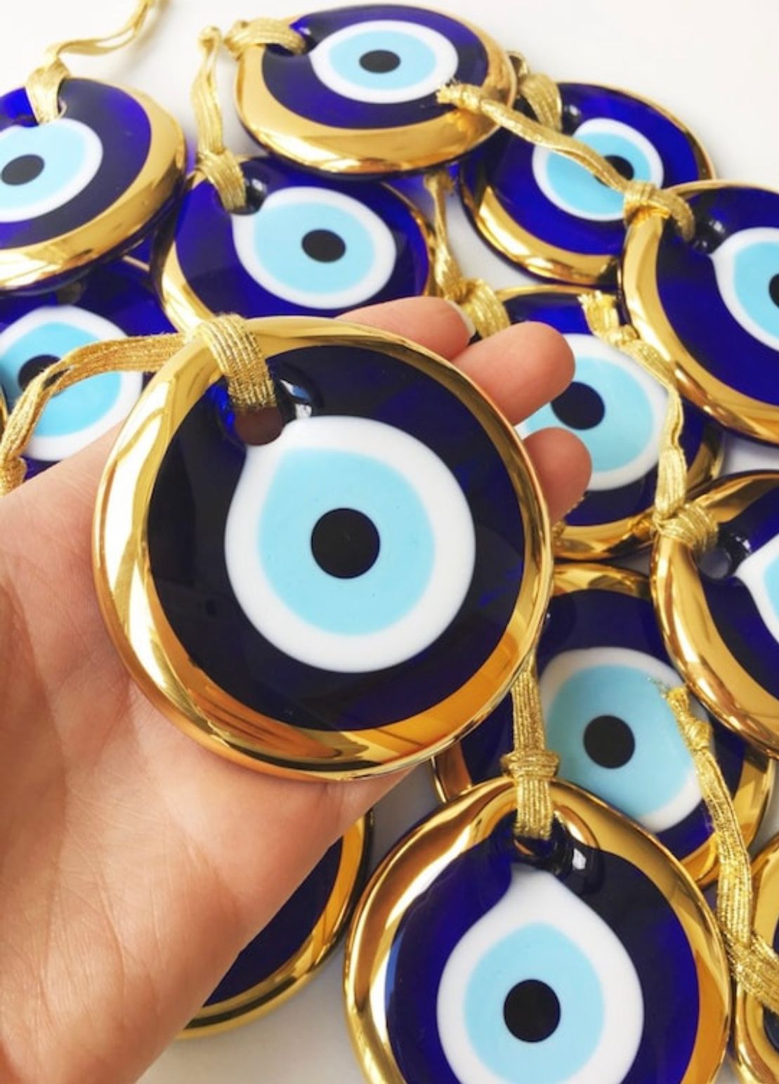 A collection of 120 handmade glass evil eye beads with gold trim and teal ribbon, showcasing their unique design and craftsmanship.