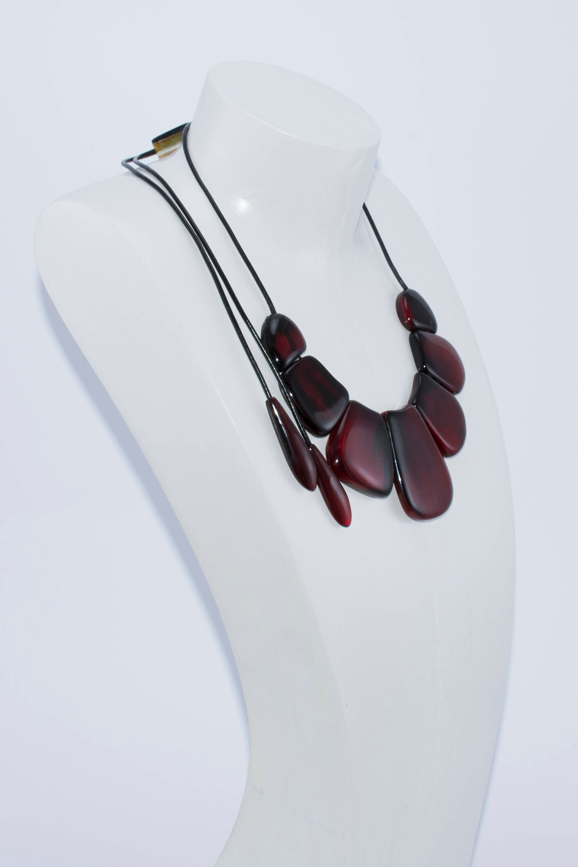 A vibrant statement red necklace made of natural horn, featuring smooth volumetric ovals and a leather cord with teardrop ends.