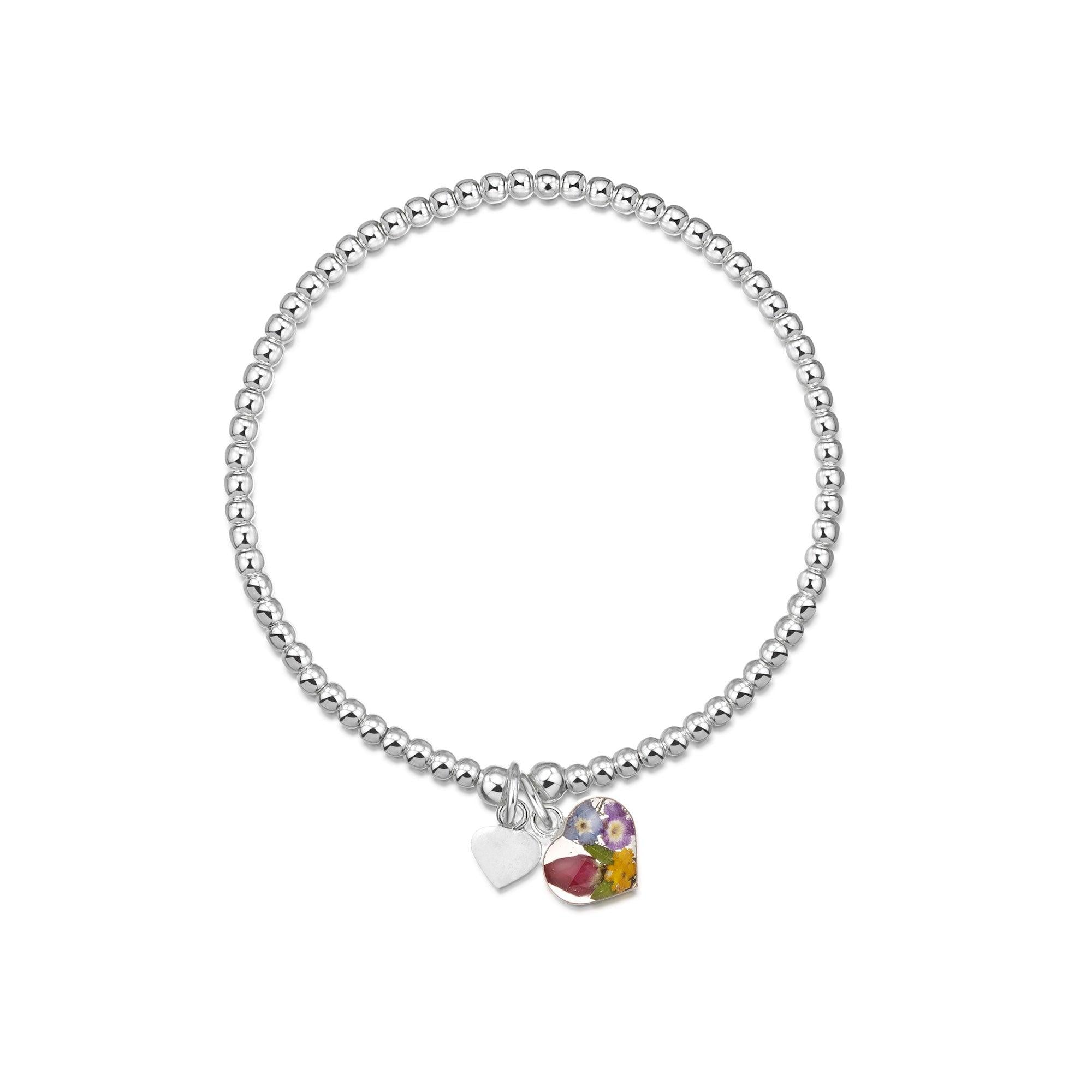 Handmade sterling silver beaded elasticated bracelet featuring a real flower charm and a sterling silver heart charm, elegantly designed.