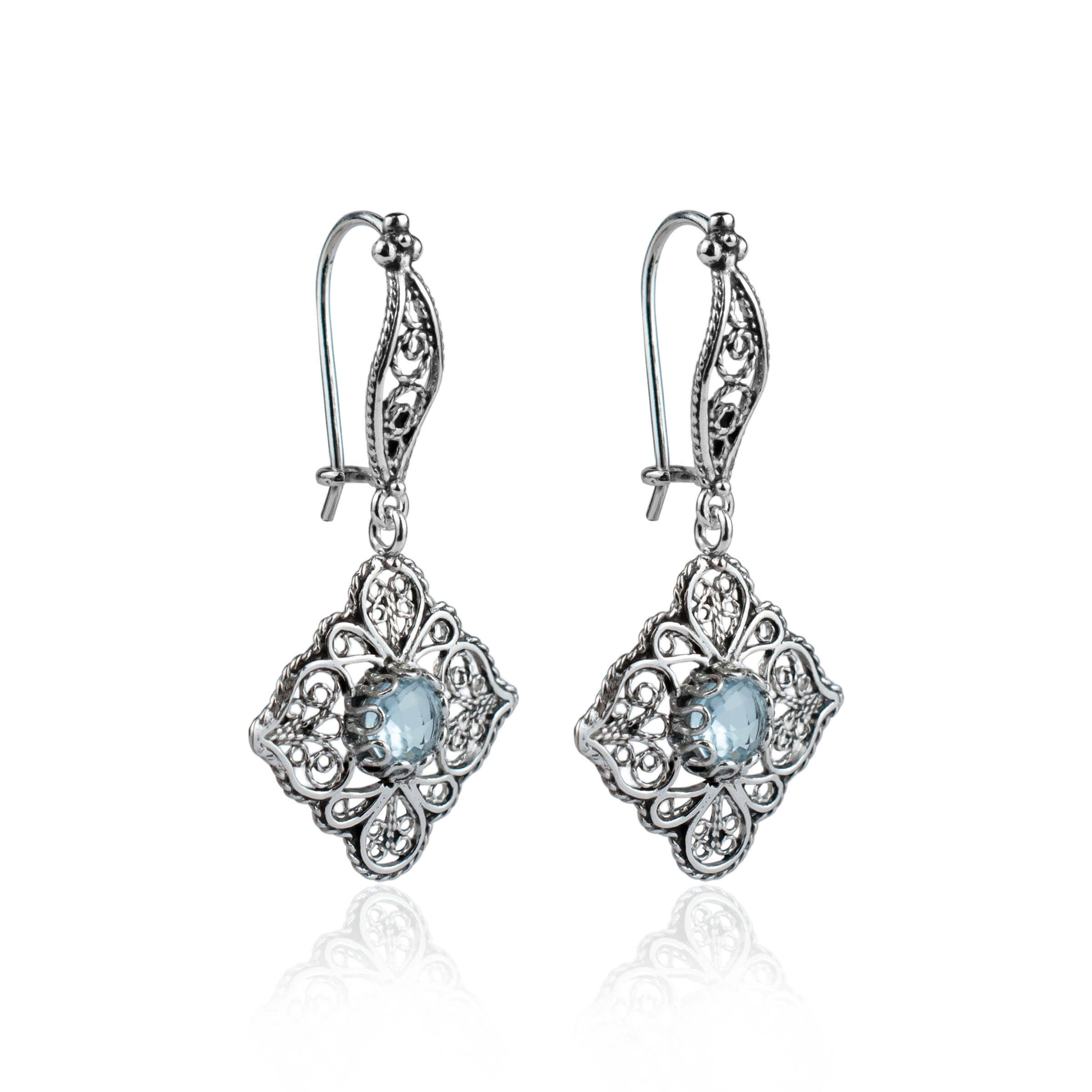 Elegant sterling silver dangle drop earrings featuring intricate filigree art and blue topaz gemstones.