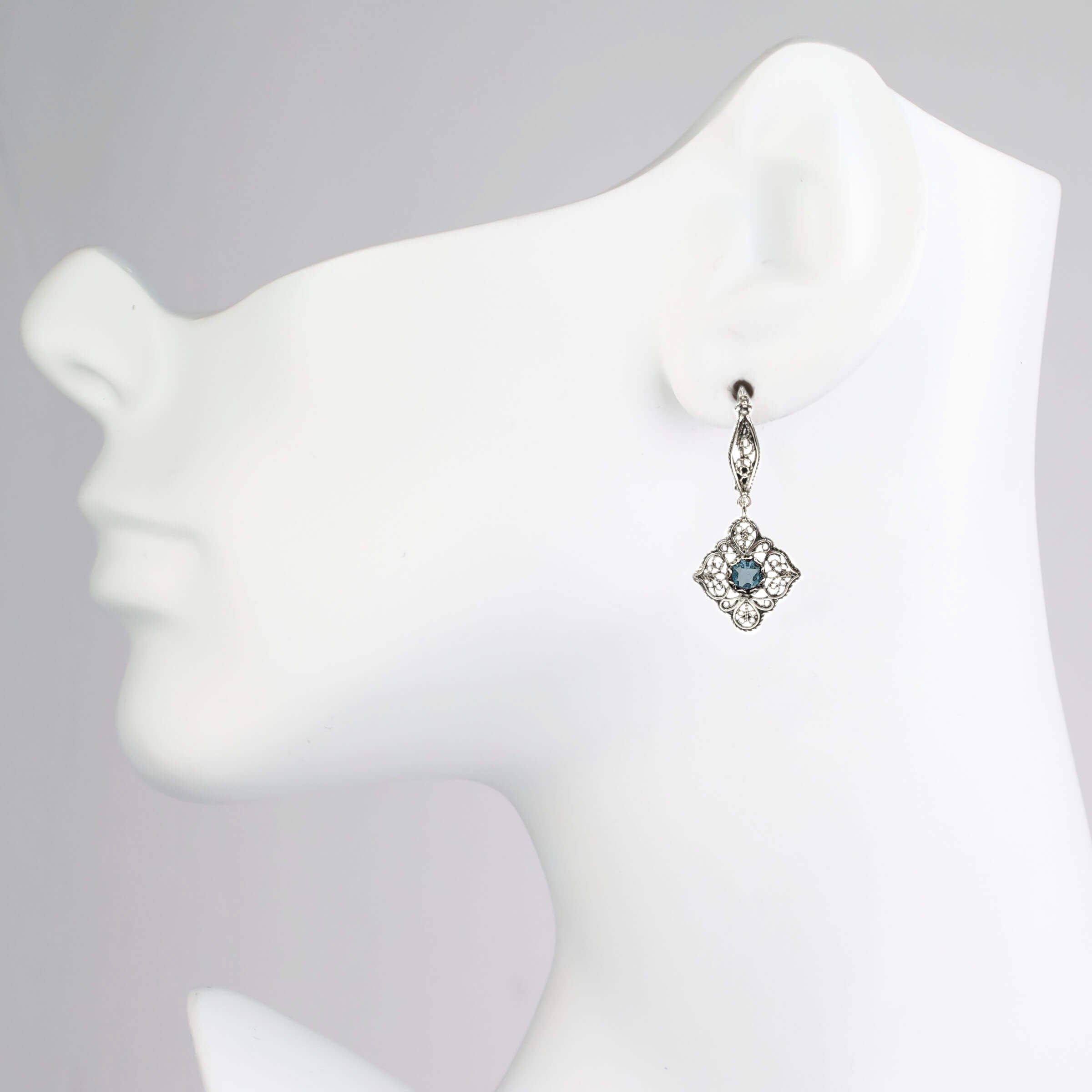 Elegant sterling silver dangle drop earrings featuring intricate filigree art and blue topaz gemstones.