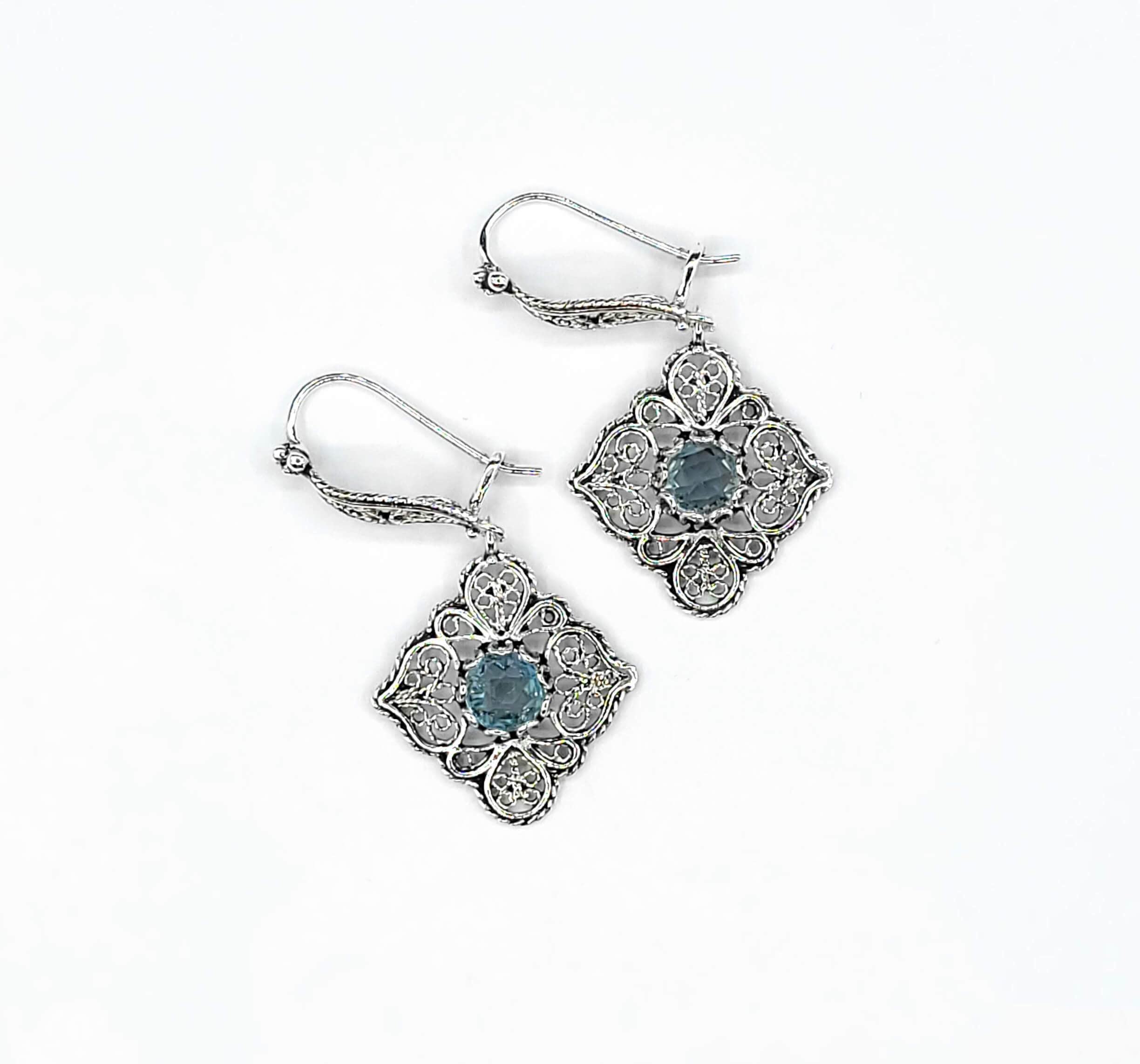 Elegant sterling silver dangle drop earrings featuring intricate filigree art and blue topaz gemstones.