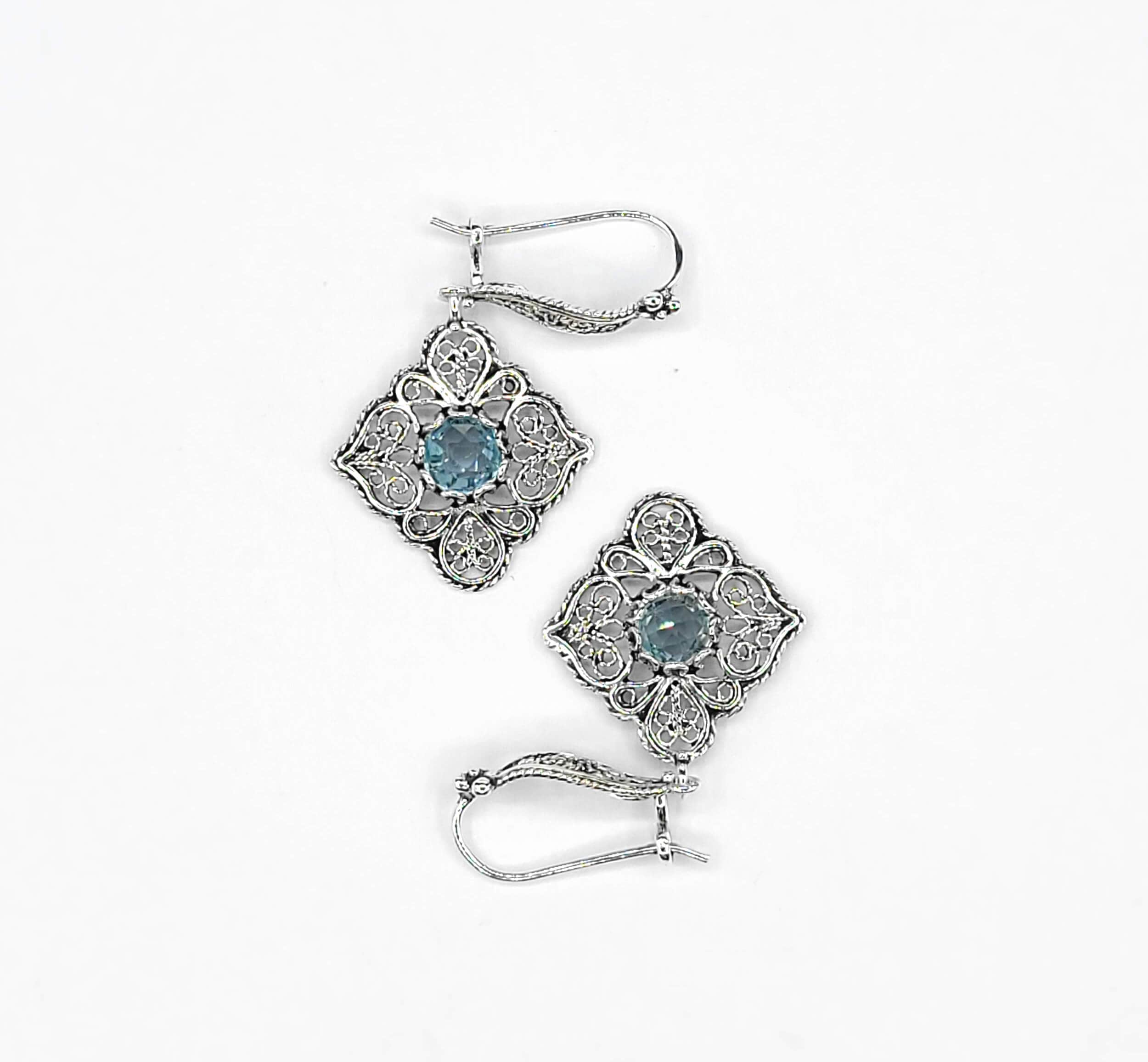 Elegant sterling silver dangle drop earrings featuring intricate filigree art and blue topaz gemstones.