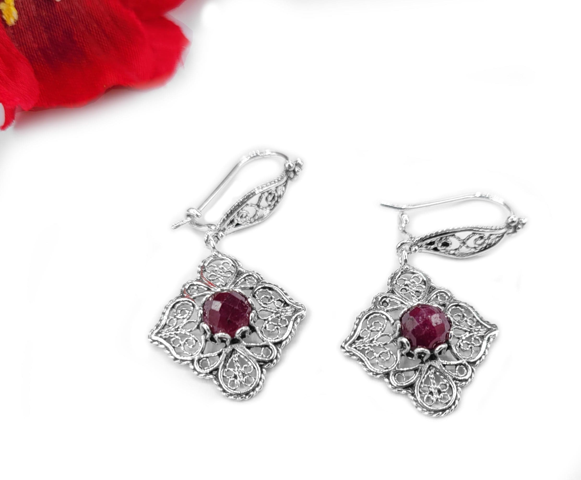 Elegant sterling silver dangle drop earrings featuring intricate filigree art and vibrant ruby corundum gemstones.