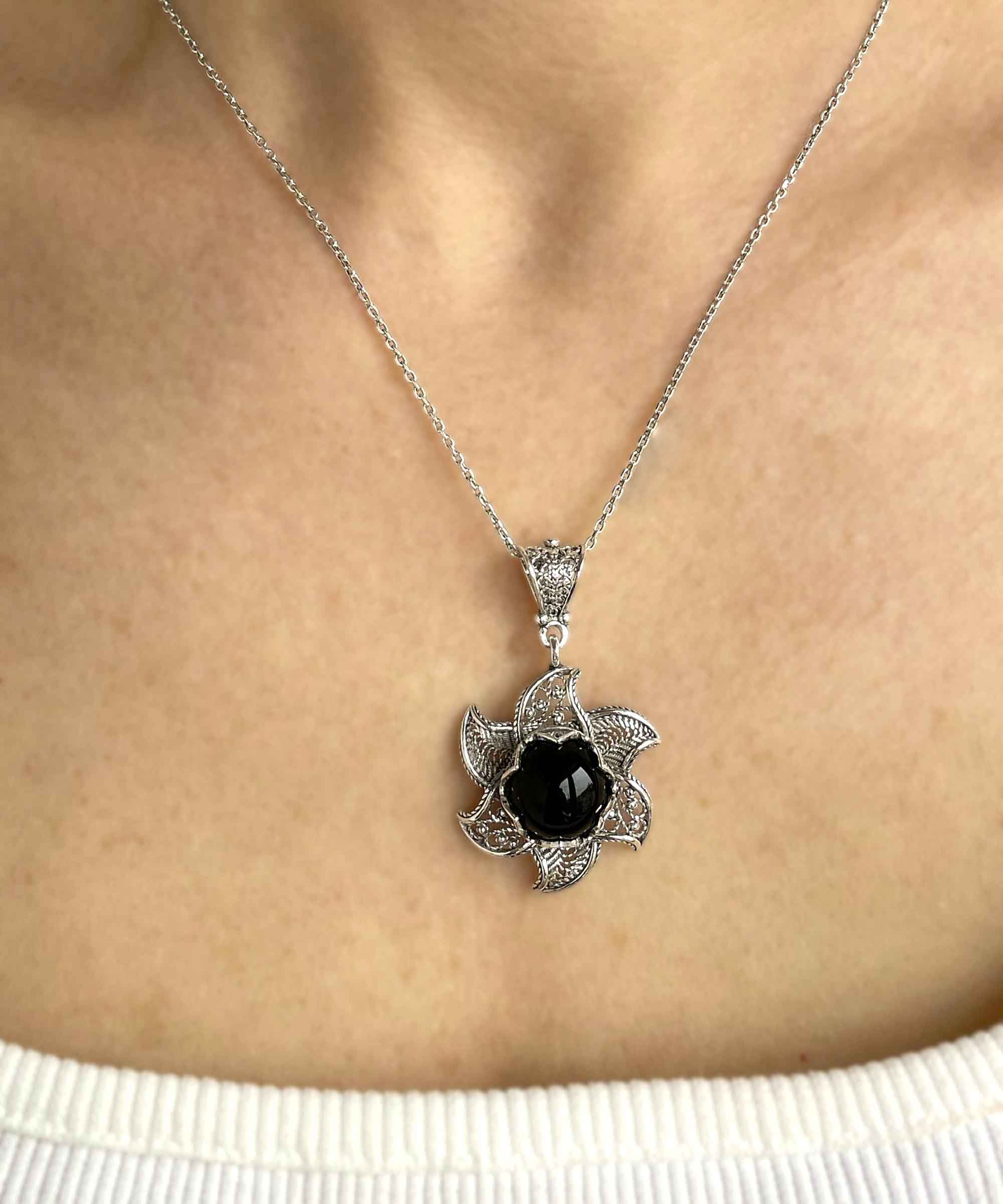 Sterling silver filigree necklace featuring a blossoming lotus flower pendant with a black onyx gemstone at the center, elegantly displayed.