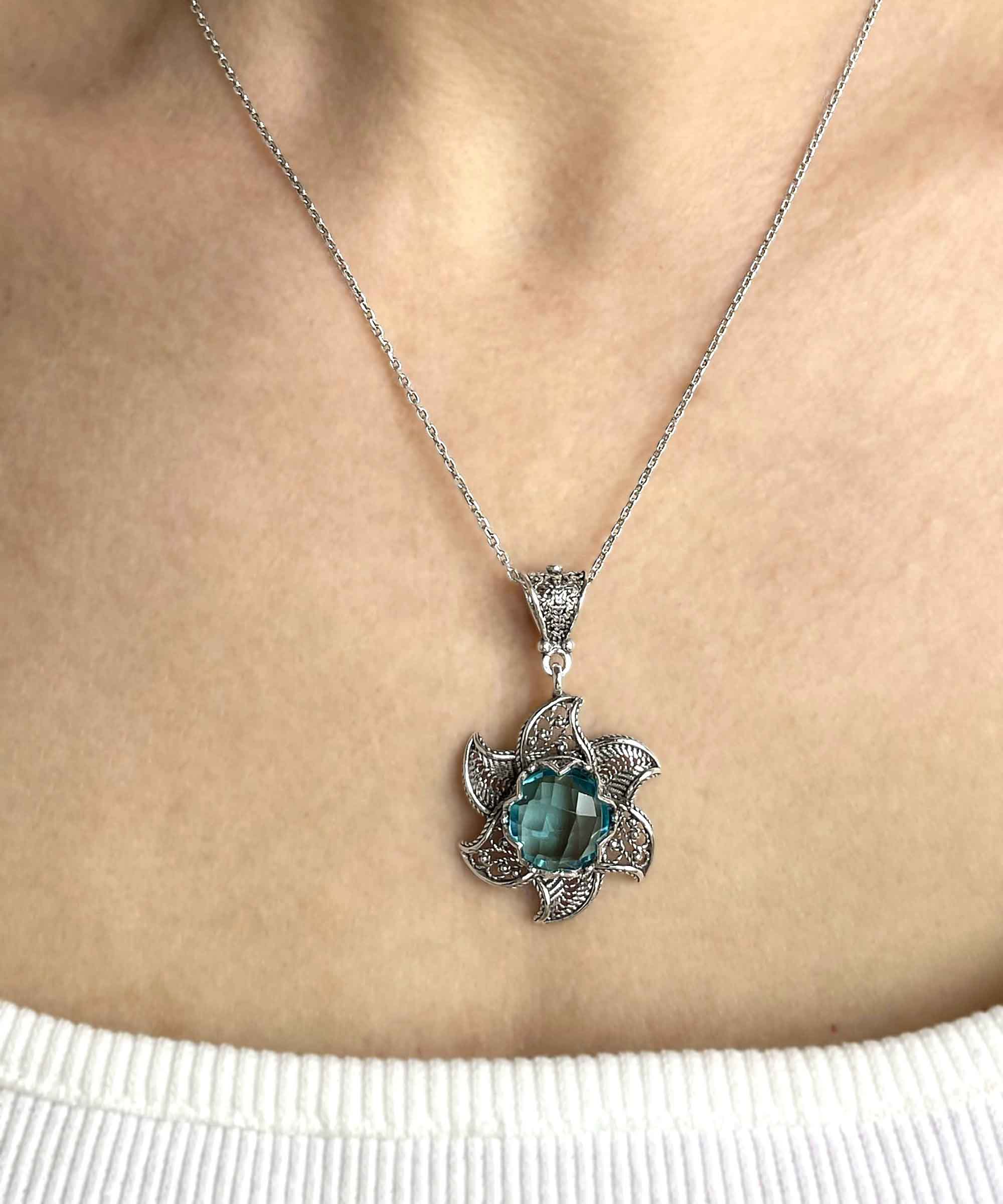 Sterling silver filigree lotus flower pendant with blue topaz gemstone, showcasing intricate design and elegant craftsmanship.