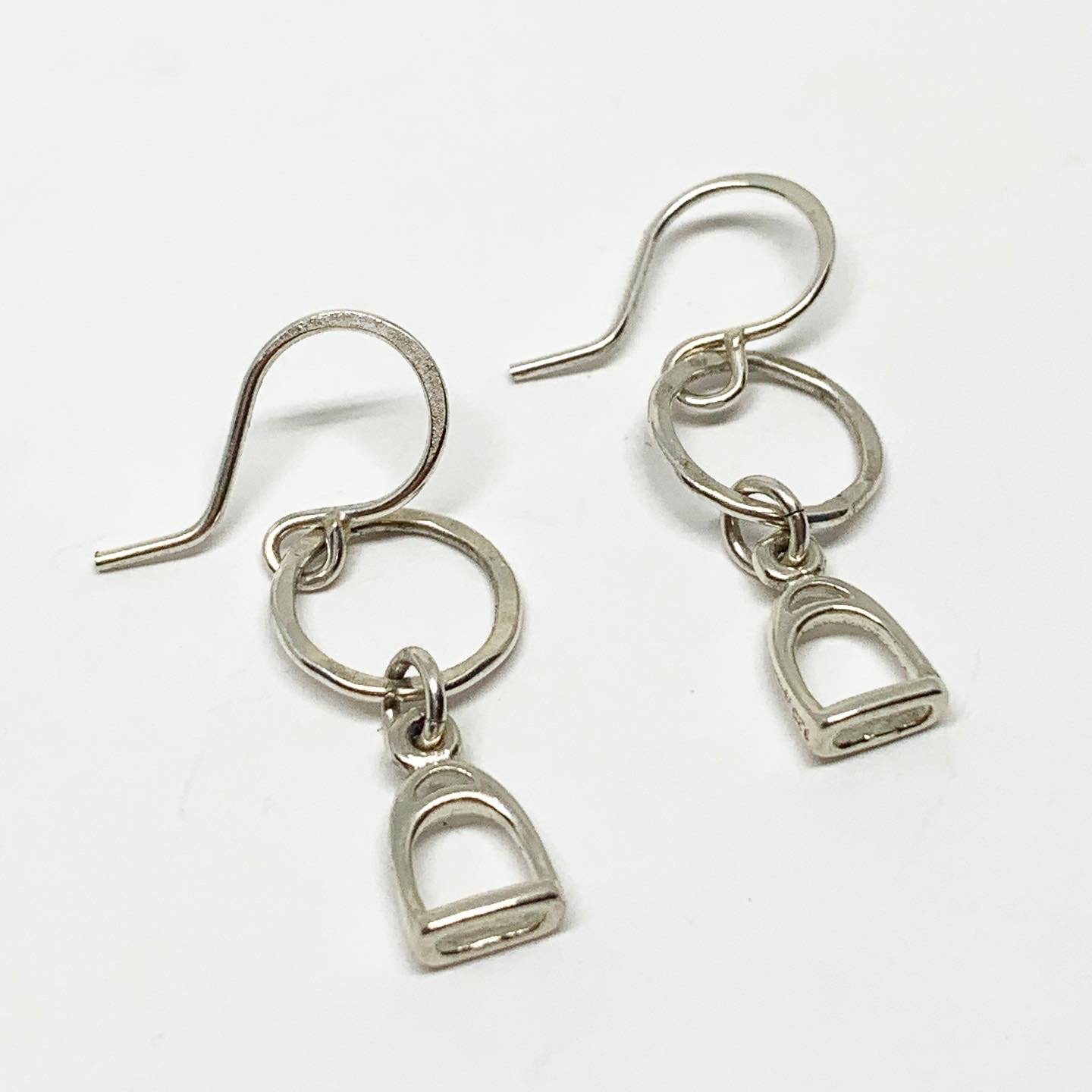 A pair of handmade Stirrup Drop Earrings featuring stirrup charms hanging from a hammered circle, crafted from recycled sterling silver.