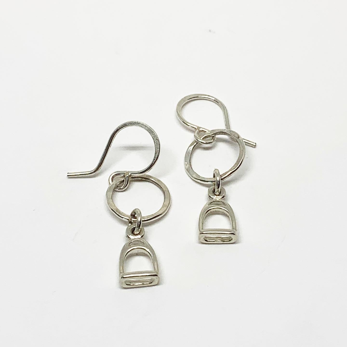 A pair of handmade Stirrup Drop Earrings featuring stirrup charms hanging from a hammered circle, crafted from recycled sterling silver.