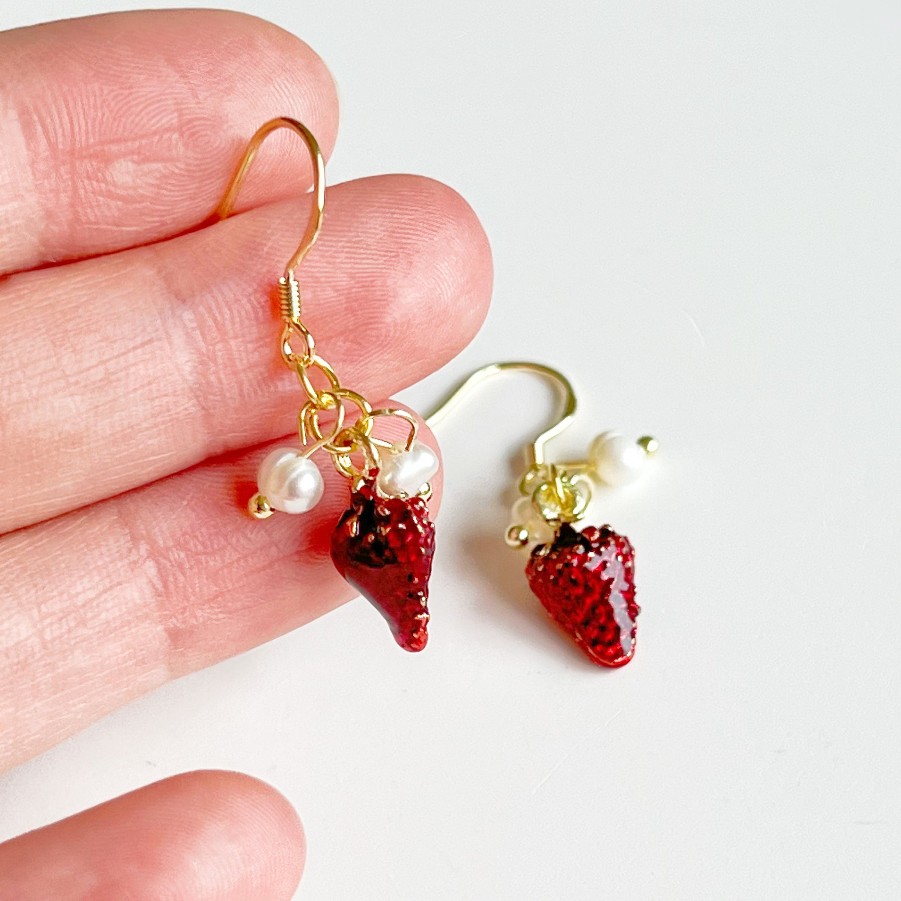 A pair of Strawberry and Pearl Mini Drop Earrings featuring vibrant strawberry designs and elegant freshwater pearls, set in gold-plated materials.