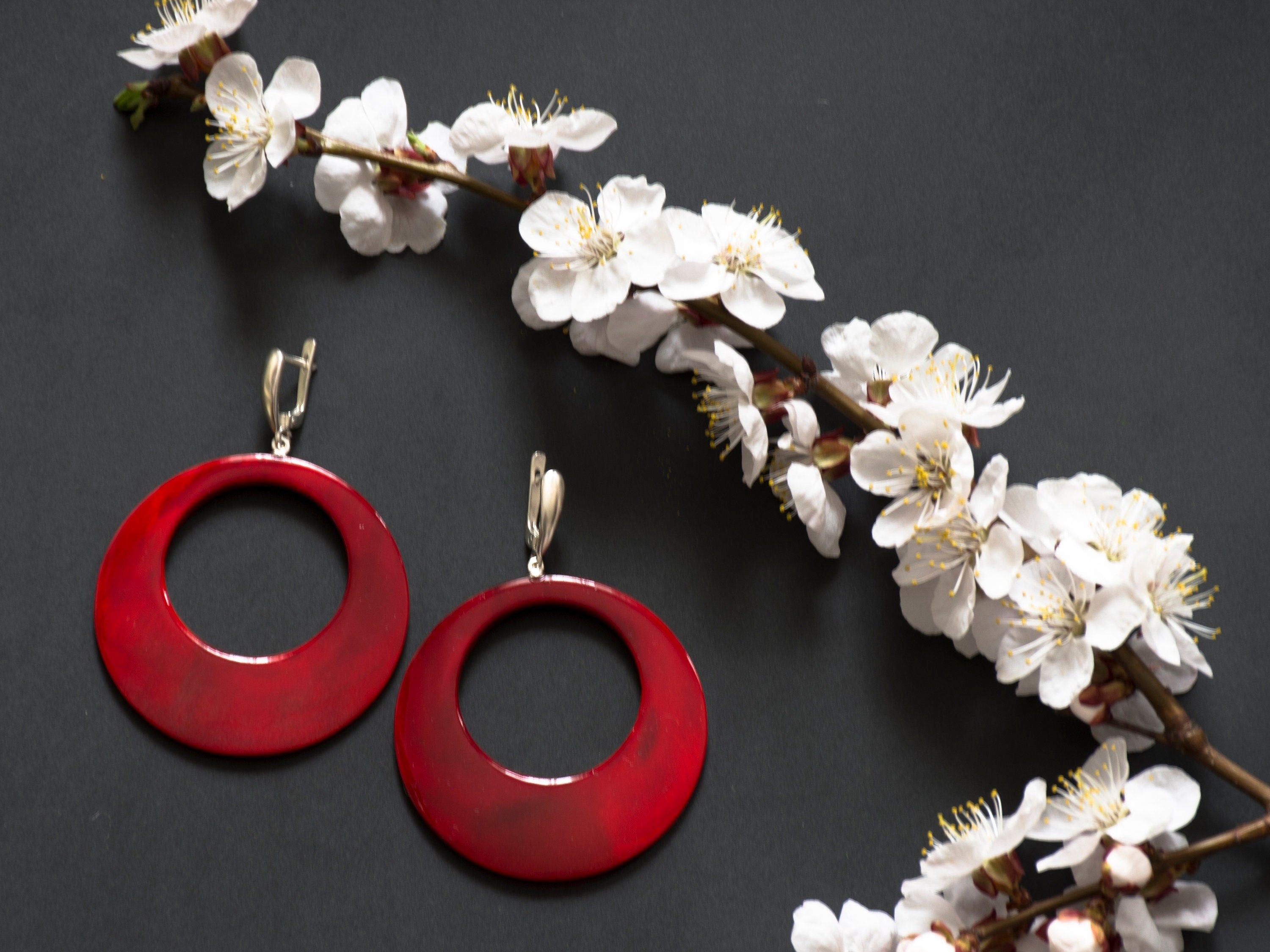 Stylish hand-carved buffalo horn earrings in red color with silver locks, showcasing intricate craftsmanship and unique design.