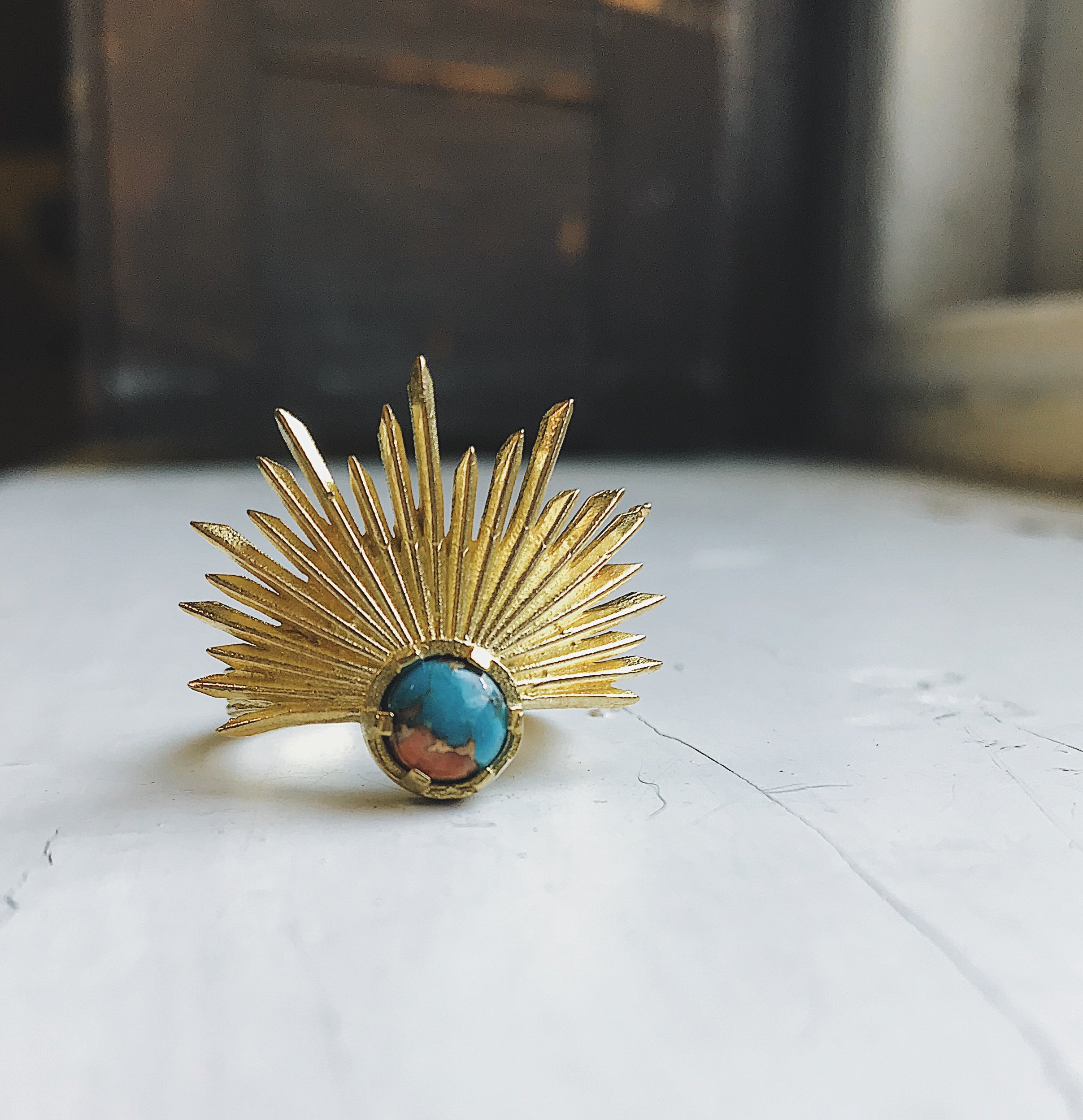 A stunning Sun Goddess Ring featuring a vibrant copper oyster turquoise stone set in a gold-tone sunburst design, showcasing its unique craftsmanship.