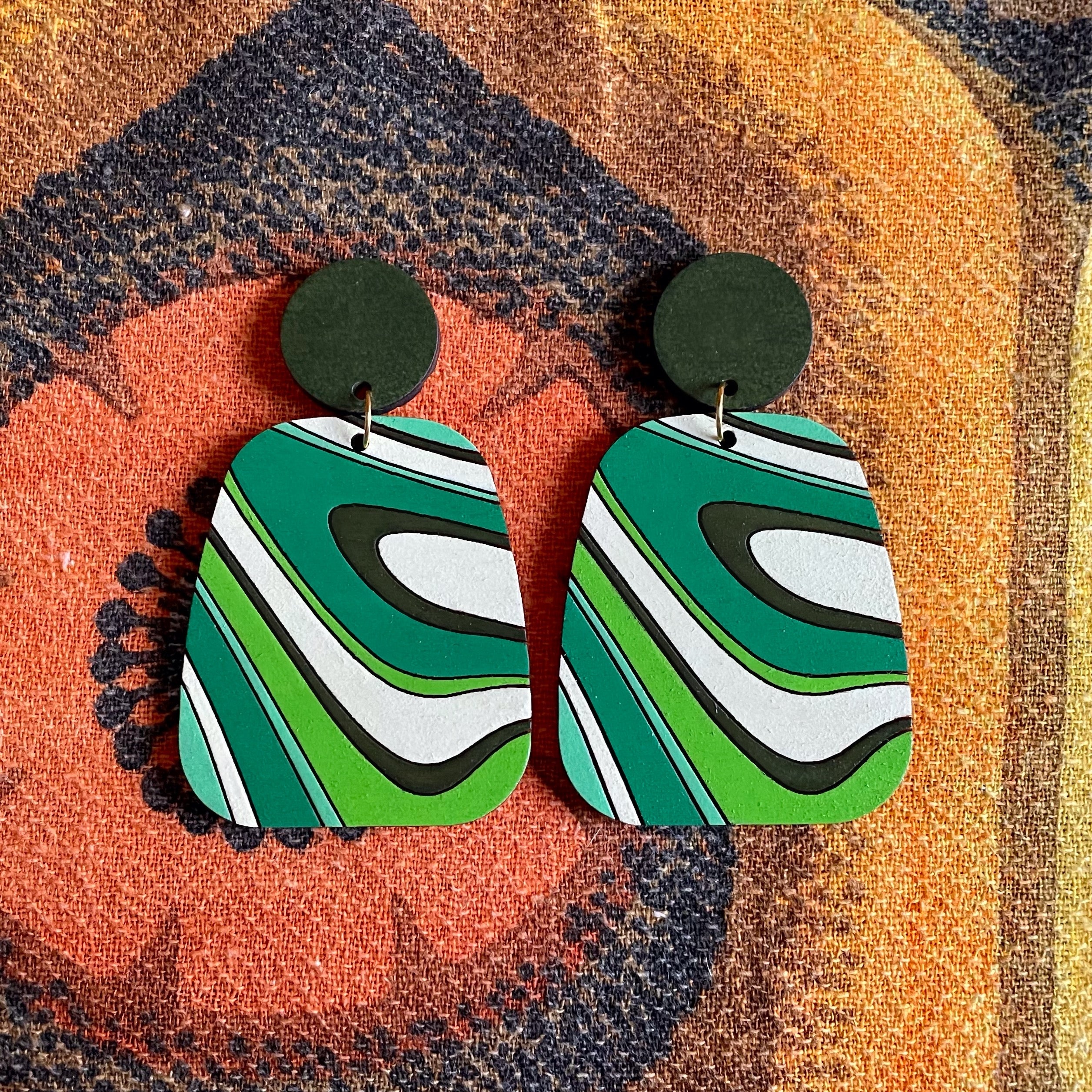 A pair of handcrafted Swirl Wood Earrings featuring intricate laser-cut designs, painted in vibrant colors, showcasing natural wood grain.