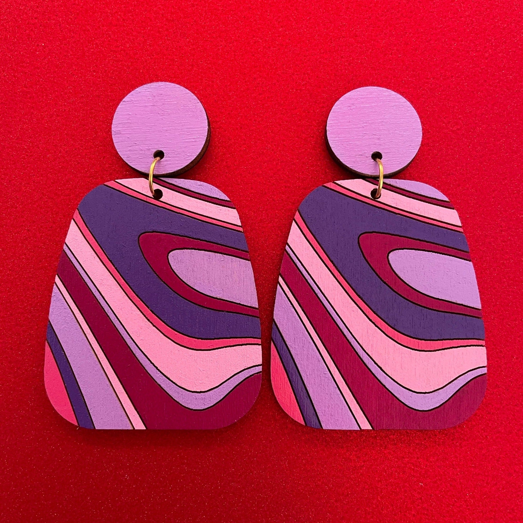 A pair of handcrafted Swirl Wood Earrings featuring intricate laser-cut designs, painted in vibrant colors, showcasing natural wood grain.