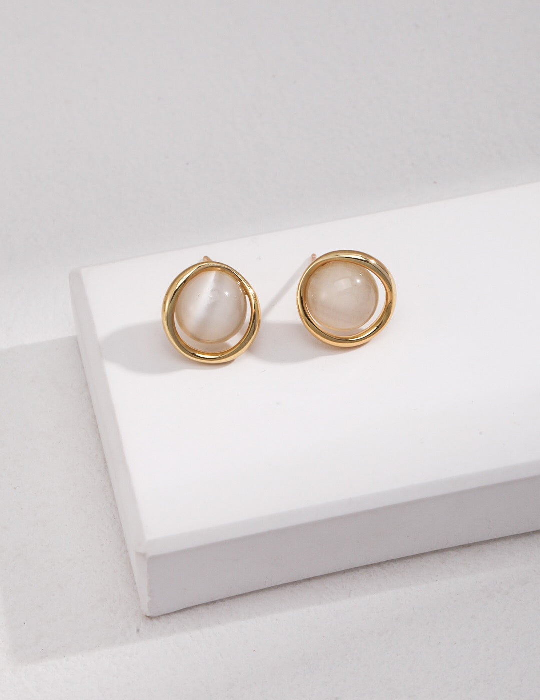 A pair of elegant synthetic cat's eye stud earrings, featuring a gold vermeil finish on sterling silver, showcasing their unique glow.