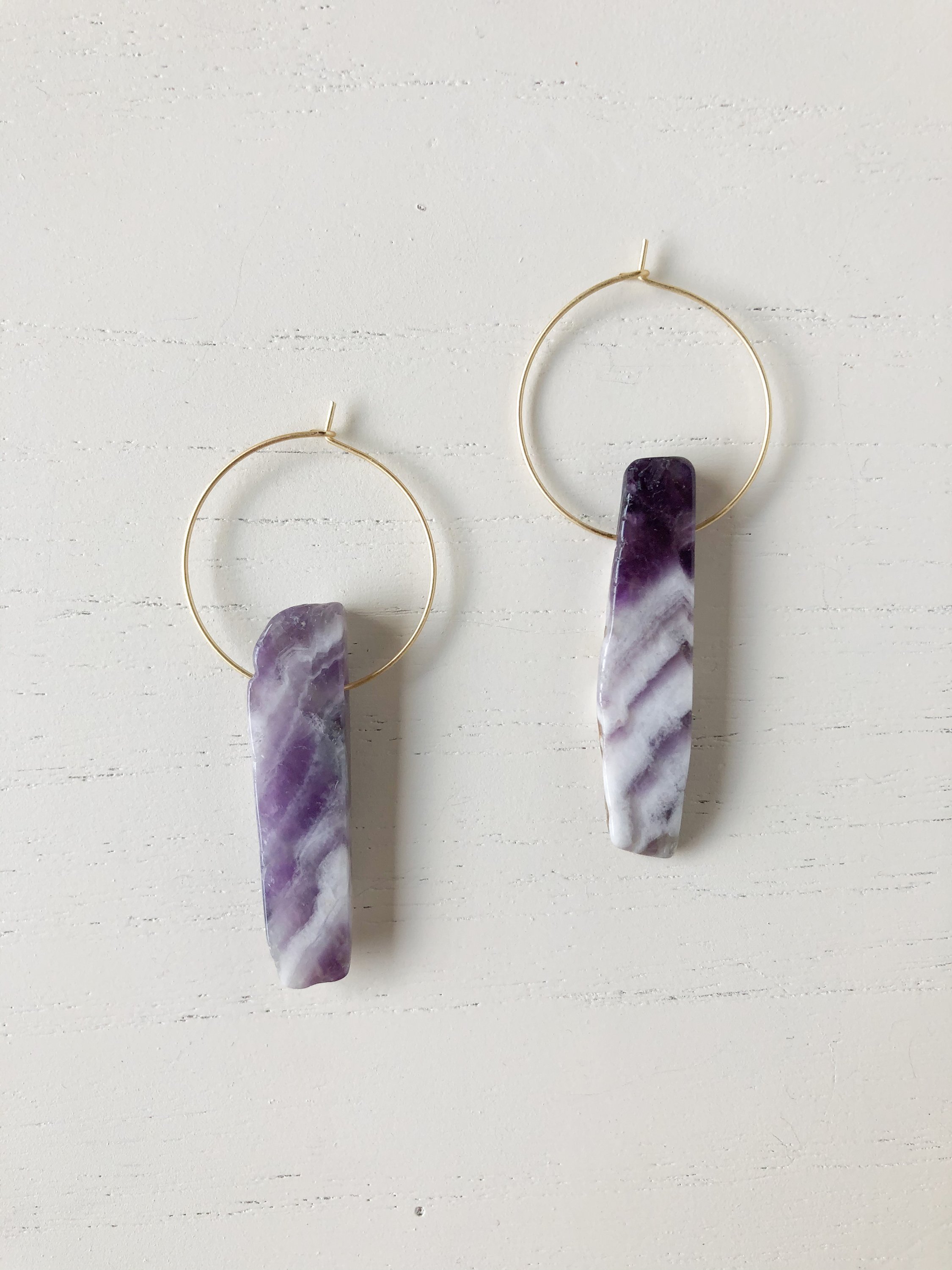 The Henley Amethyst earrings featuring a brass hoop and a genuine amethyst stone, showcasing their unique design and spiritual significance.