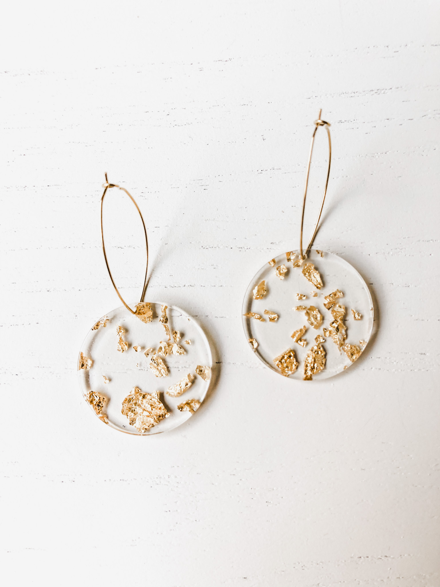 The Maddy Roundies Gold earrings featuring brass hoops with clear acrylic and gold flake resin details, elegantly designed for stylish wear.