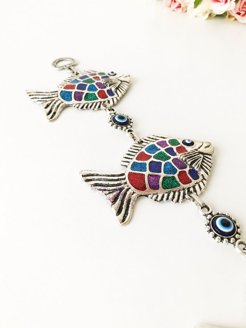 Three fish evil eye wall hanging featuring blue evil eye bead and metal fish charms, symbolizing protection and good luck.