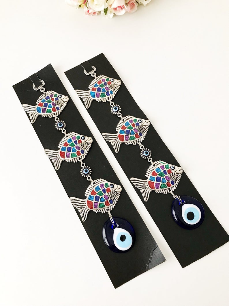 Three fish evil eye wall hanging featuring blue evil eye bead and metal fish charms, symbolizing protection and good luck.