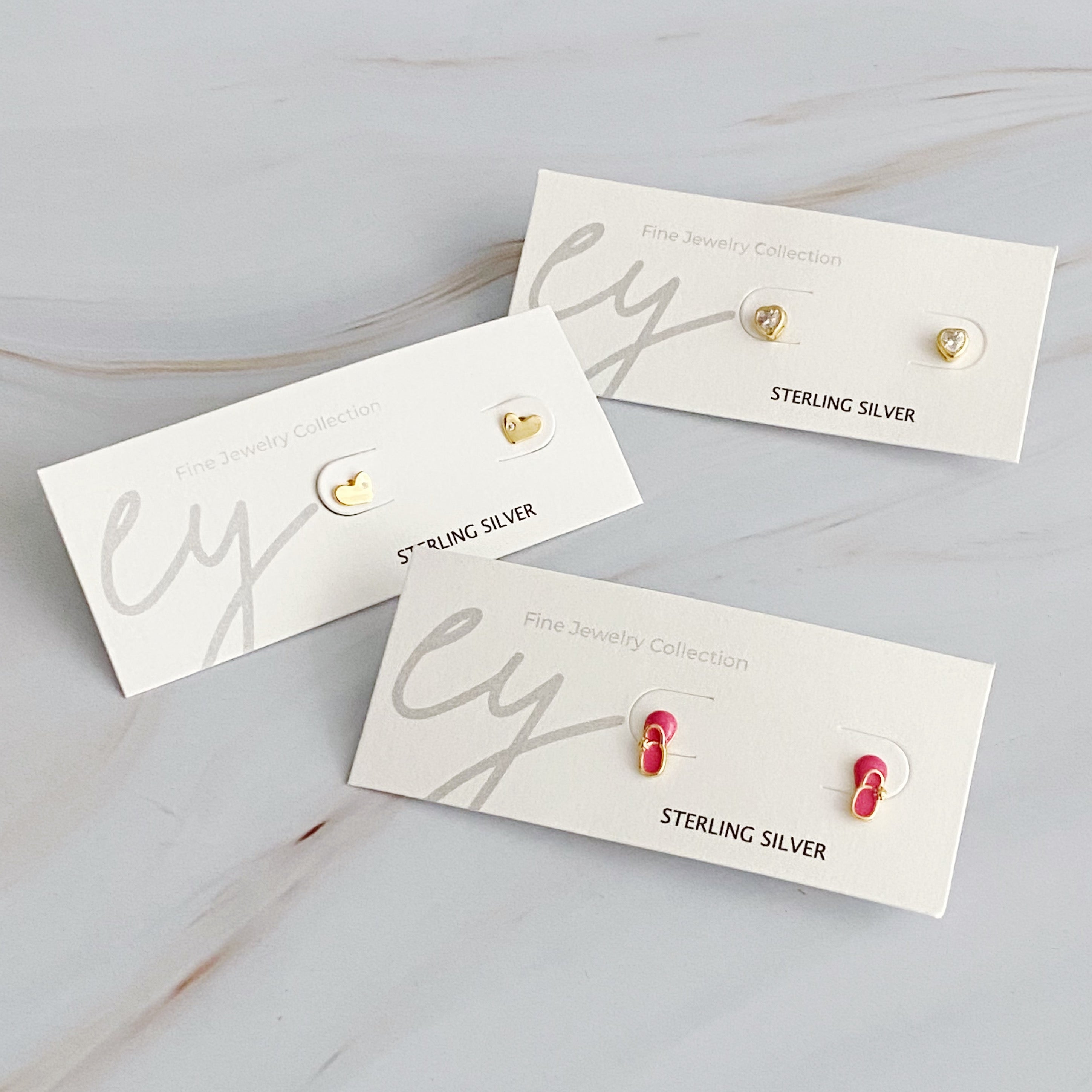 Tiny Shape Tiny Stud Sterling Silver Earrings featuring heart and flip flop designs, elegantly displayed on a logo card.