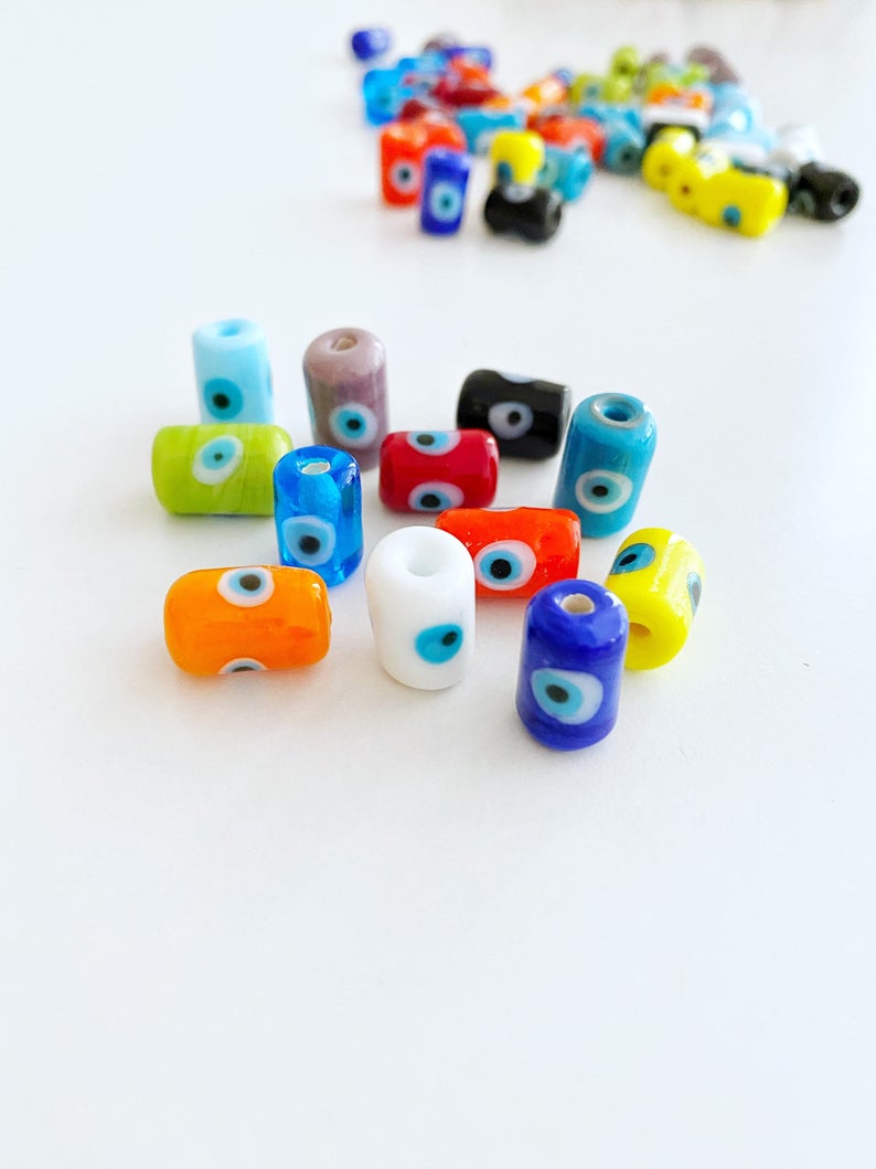 A collection of colorful Tube Evil Eye Murano Beads in various shades including blue, red, and green, showcasing their unique designs and craftsmanship.